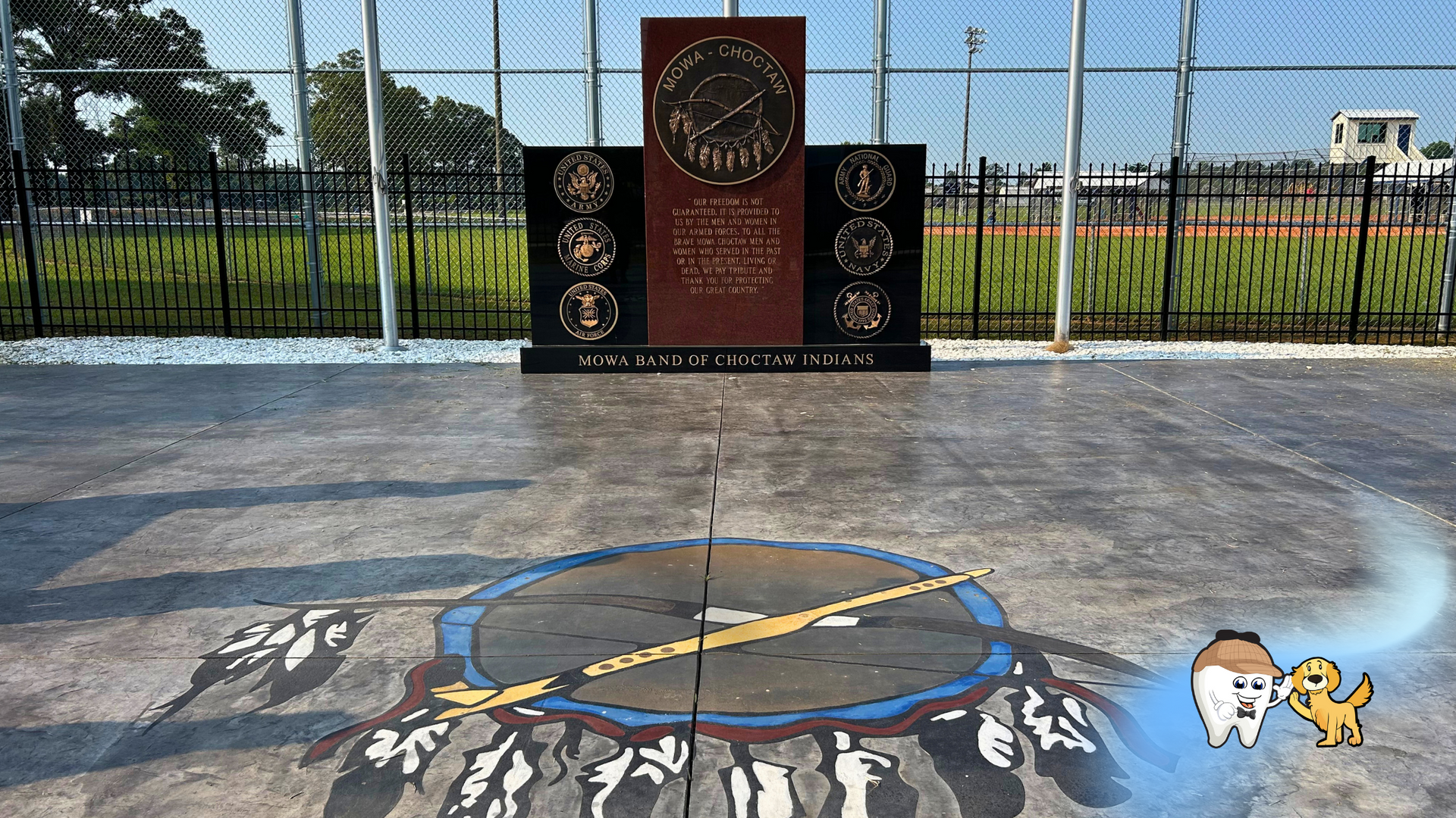 A clock is painted on the ground in front of a fence.