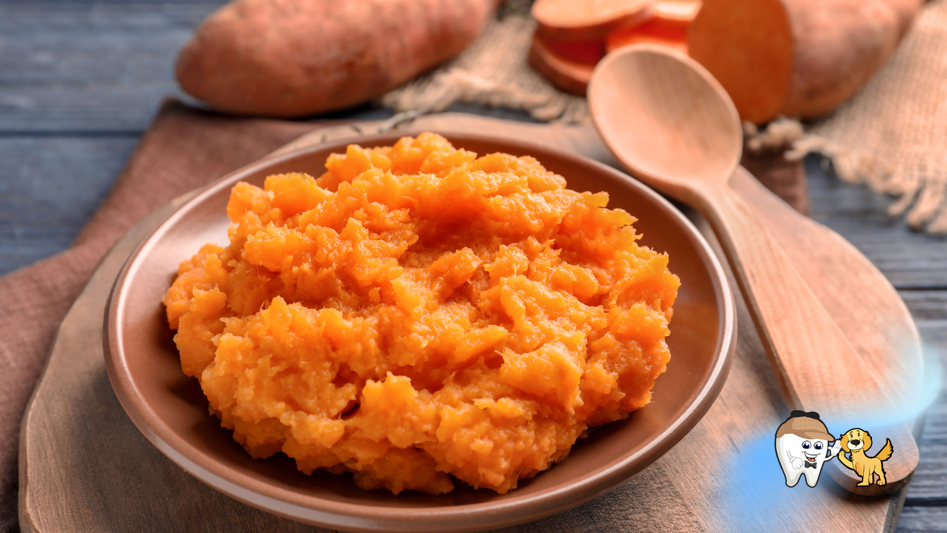 Mashed sweet potatoes in a brown bowl with a wooden spoon and whole sweet potatoes in the background.