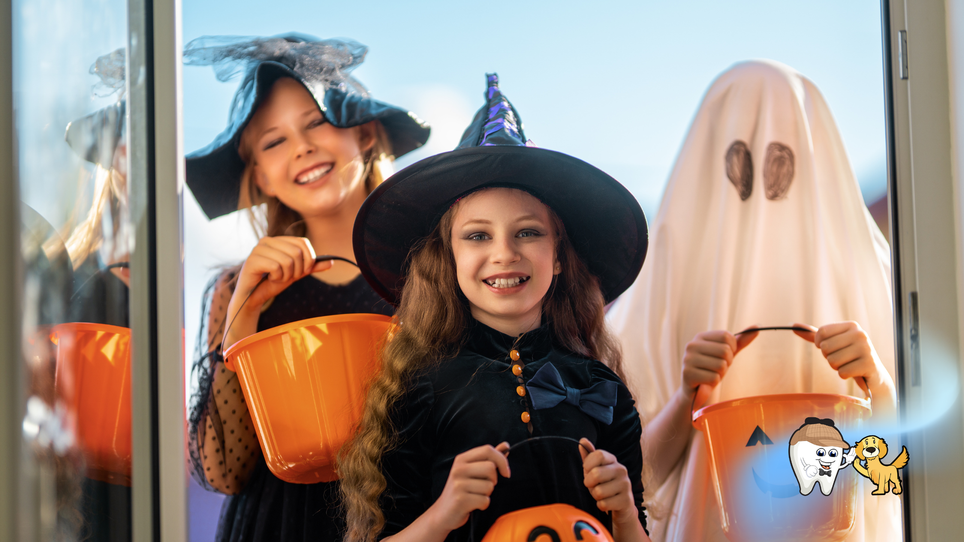 Three children in Halloween costumes: witch, ghost, and another witch holding treat buckets by a doorway.