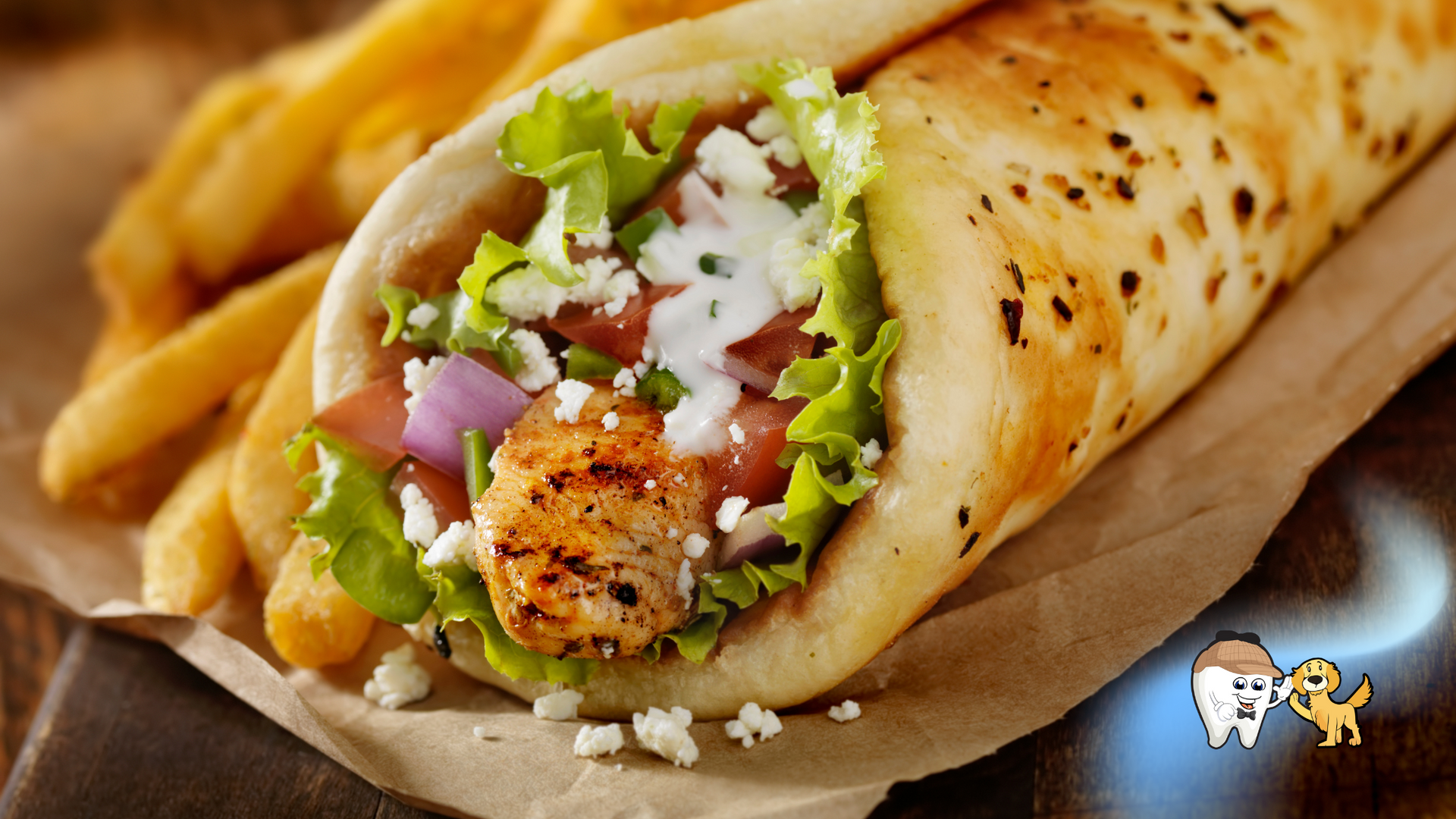 Gyro sandwich with fries, featuring grilled chicken, lettuce, tomatoes, red onion, and feta cheese in a pita.