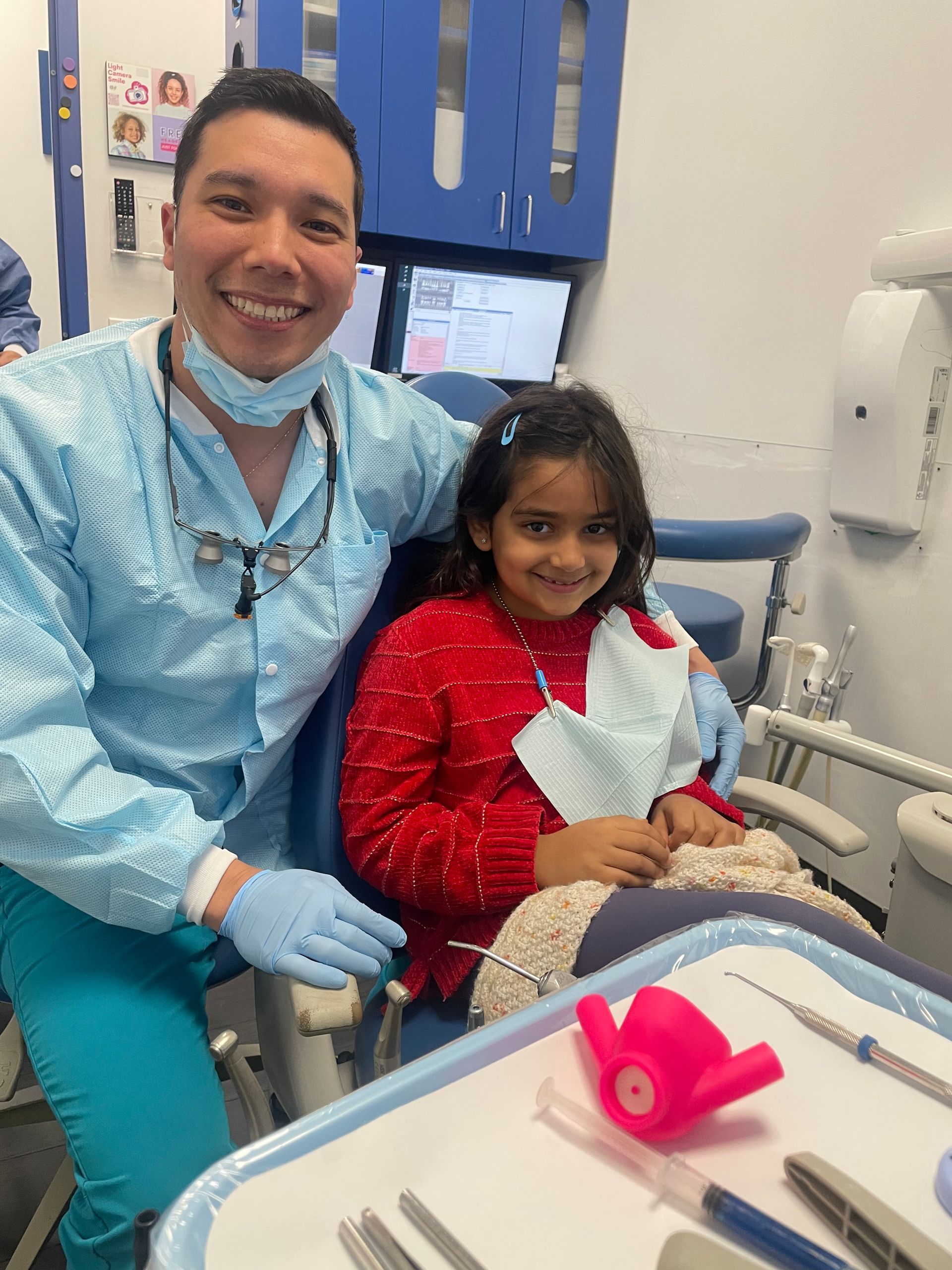 a dentist smiles while a little girl sits in a dental chair | Dr. John Ding Pediatric Dentist | Cavity Detective | Best Pediatric Dentist In Tinton Falls, NJ