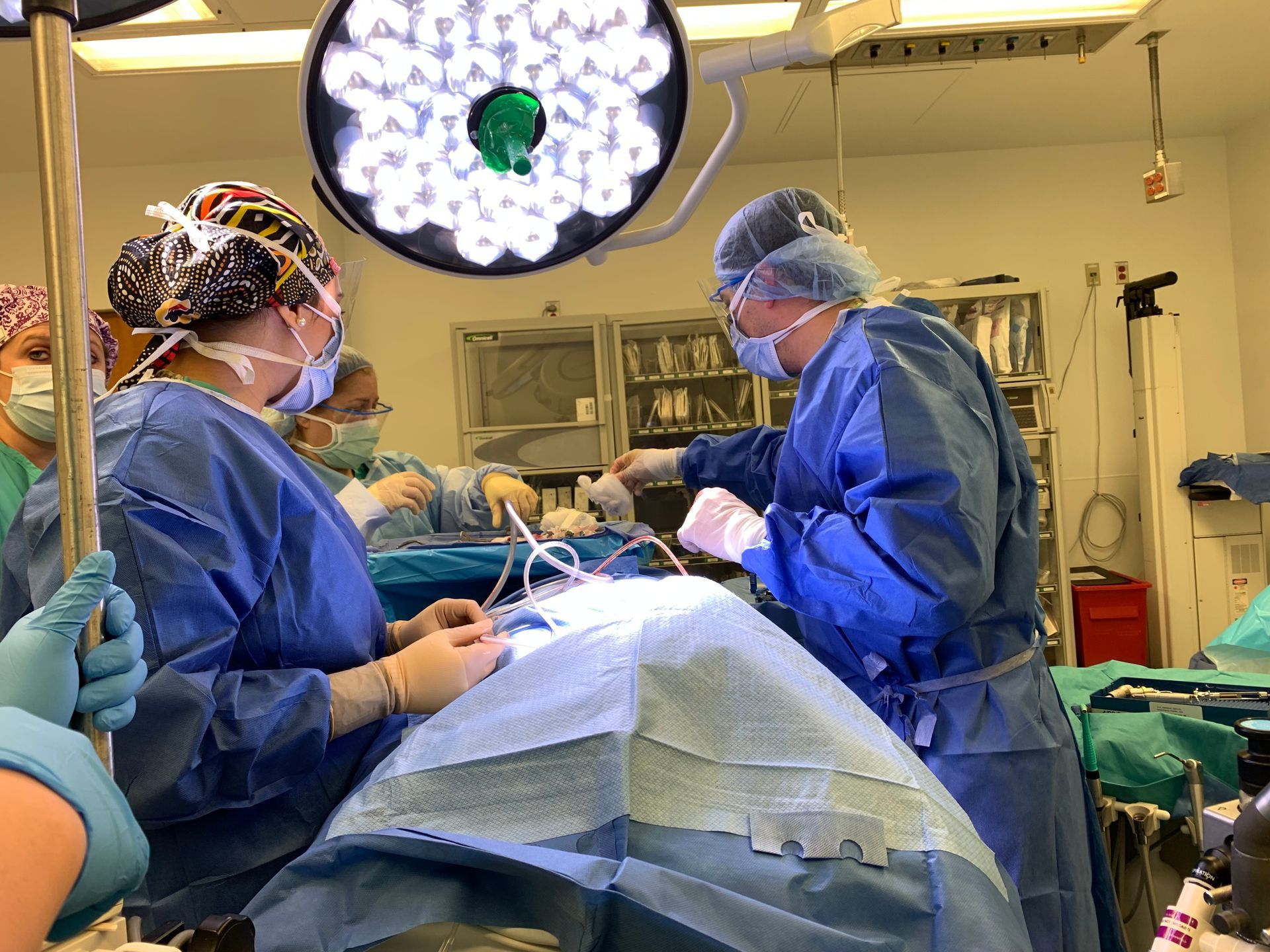 Medical staff in surgical scrubs performing an operation in an operating room, under bright lights.