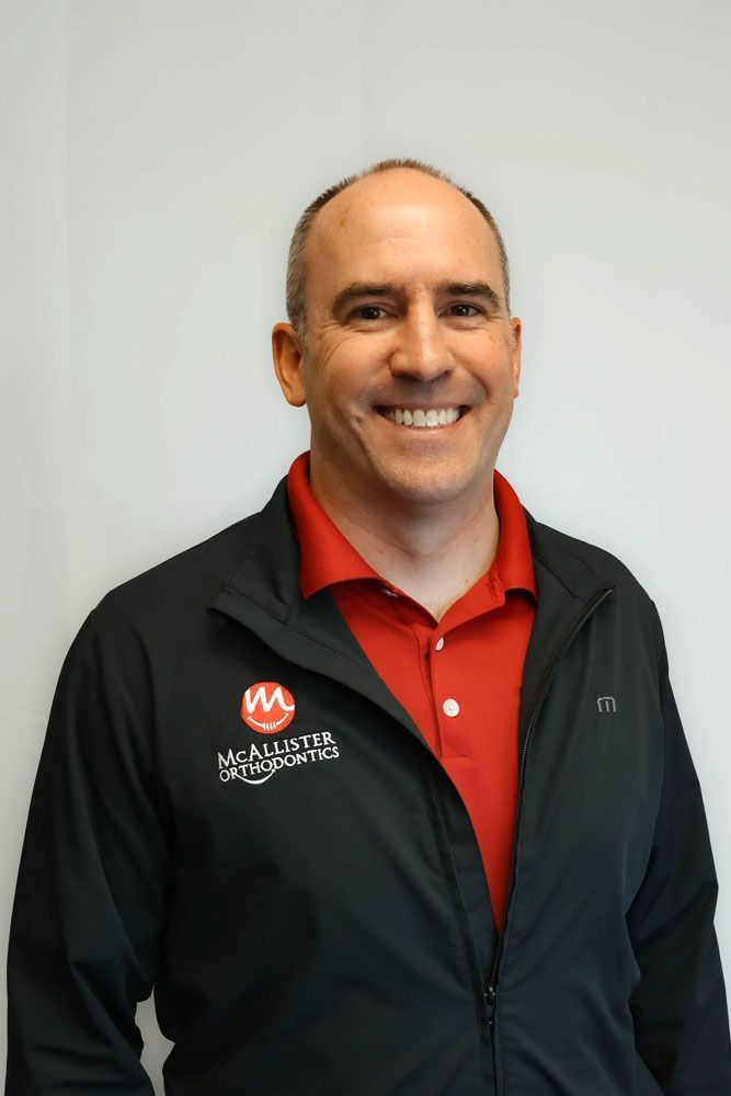 A man wearing a black jacket and a red shirt is smiling for the camera.