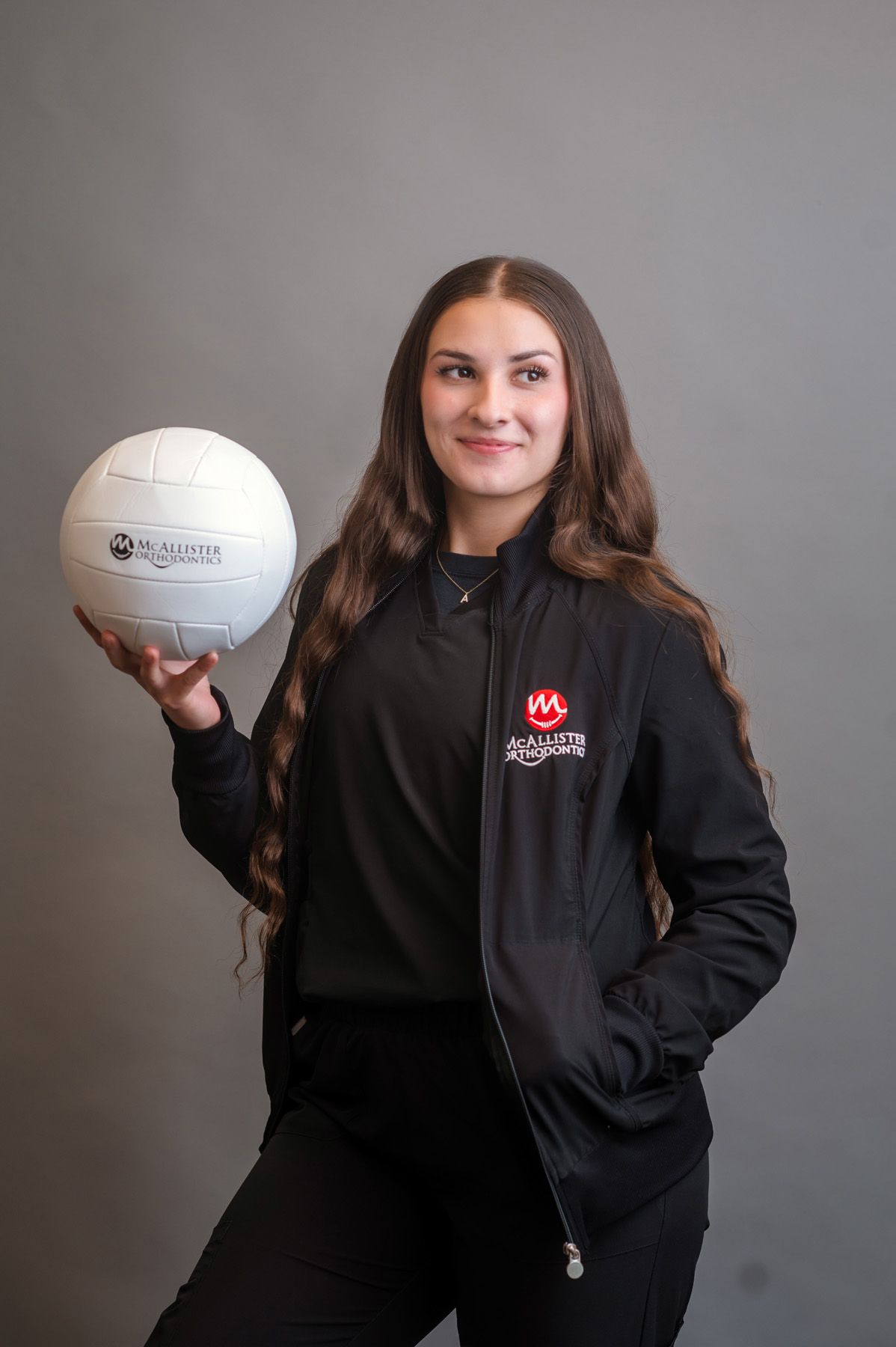 A woman in a black jacket is holding a volleyball in her hands.