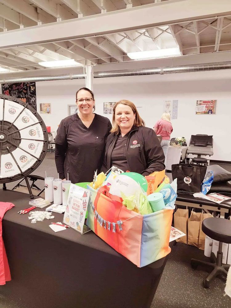 Two women are standing next to a table with a bag of gifts on it.