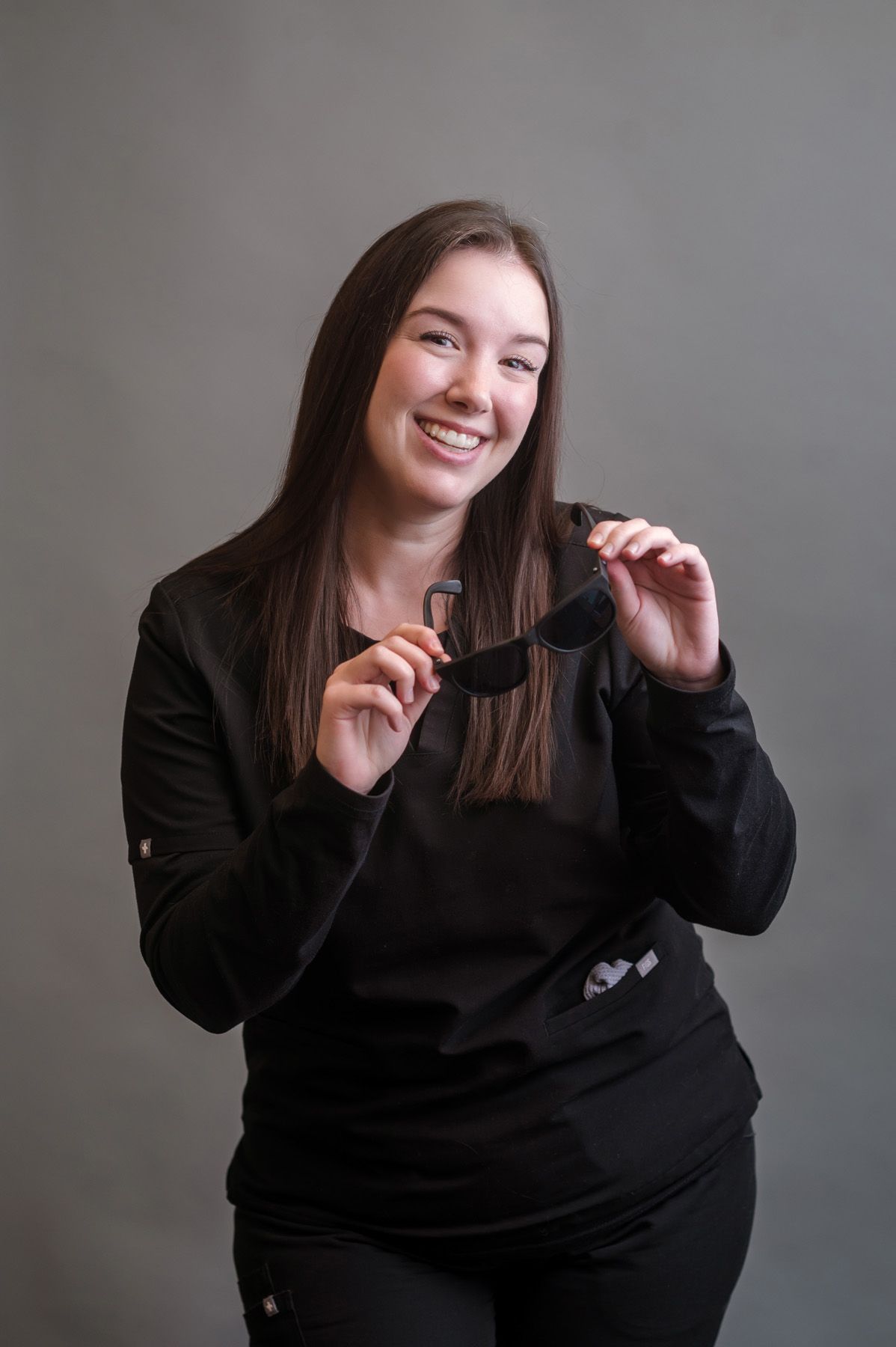 A woman in a black jacket is standing with her hands on her hips and smiling.