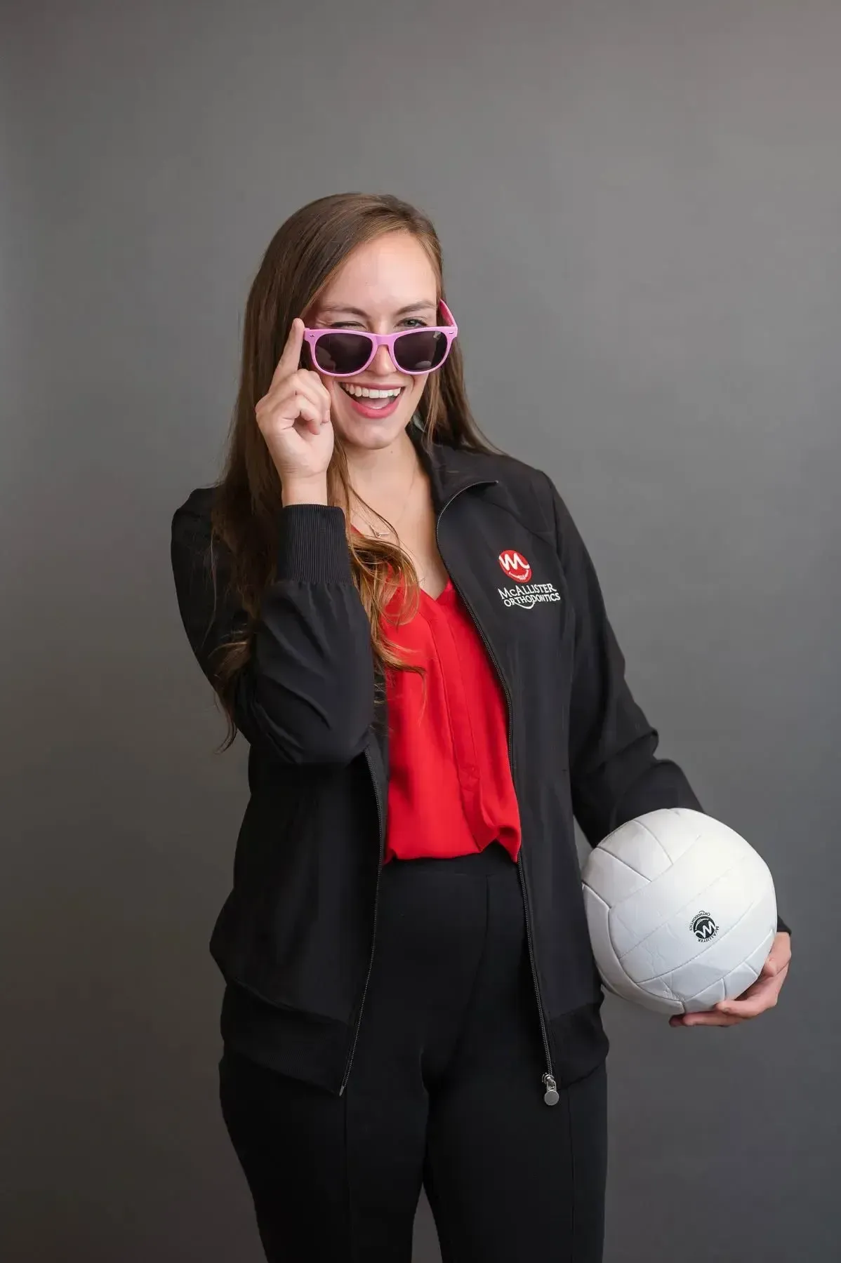 A picture of a woman in McAllister uniform wearing sunglasses and holding a volleyball.