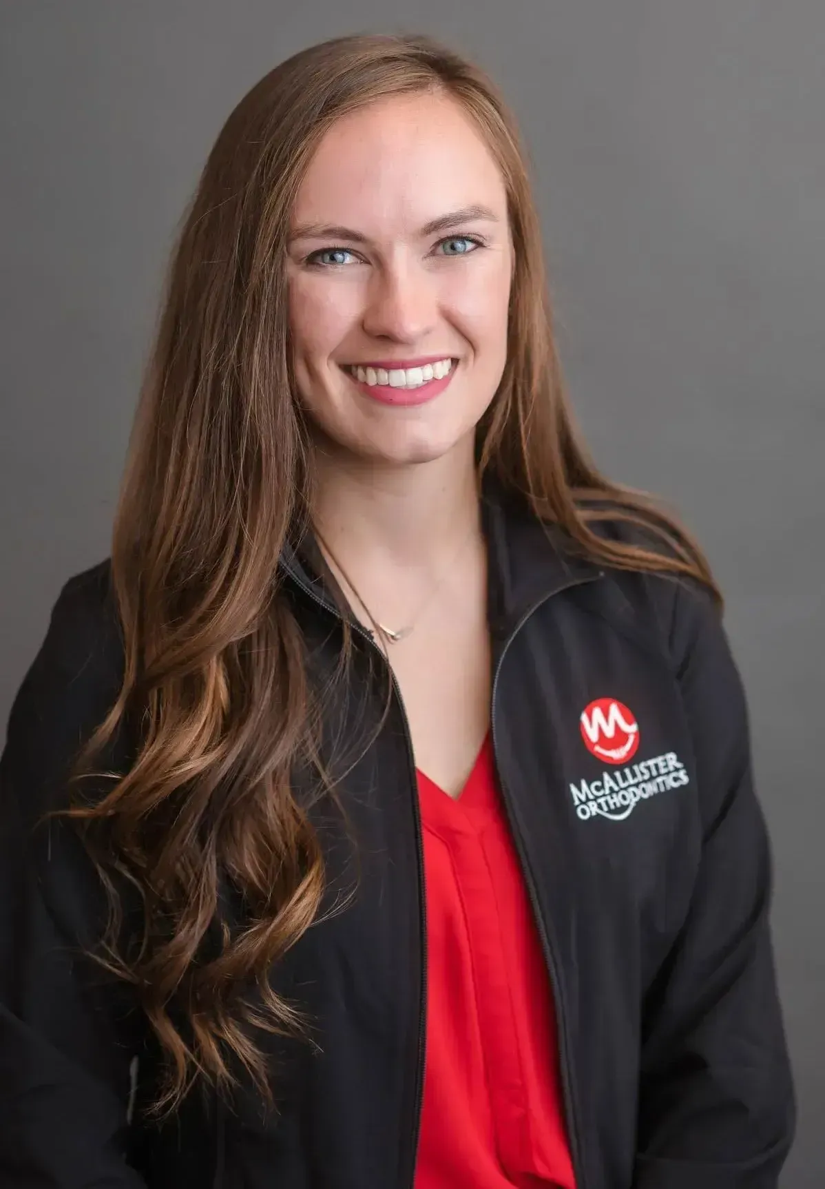 A woman wearing a black jacket and a red shirt is smiling for the camera.