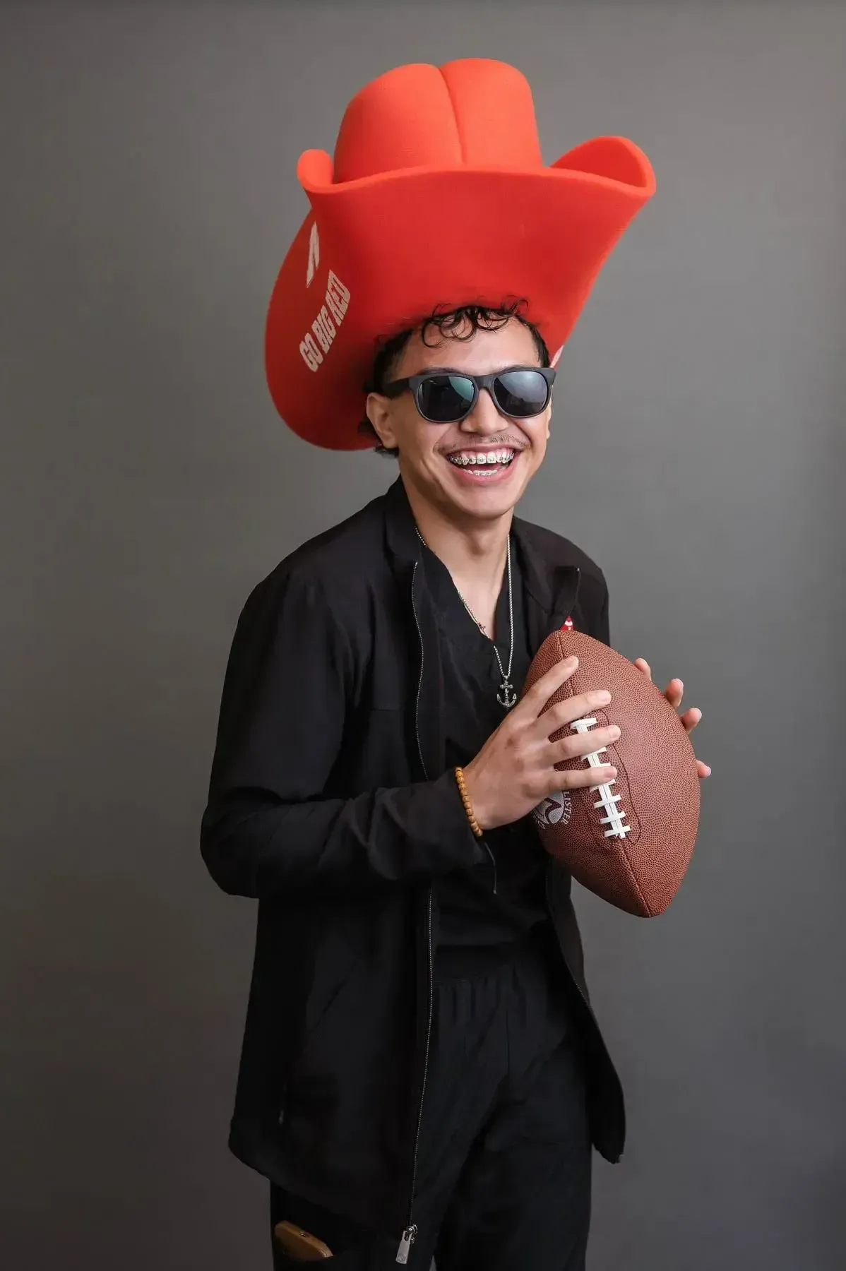 A man wearing a cowboy hat and sunglasses is holding a football.