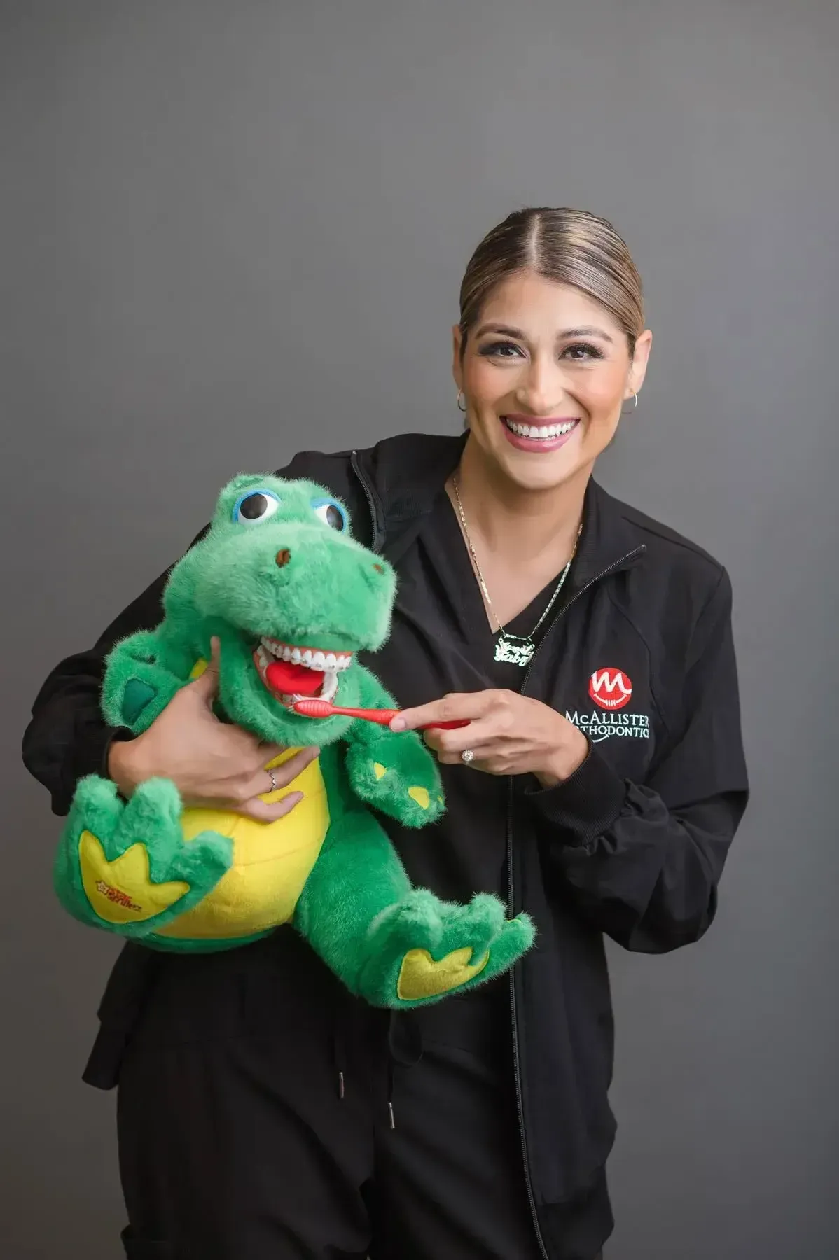 A woman is holding a stuffed dinosaur with a toothbrush in its mouth.