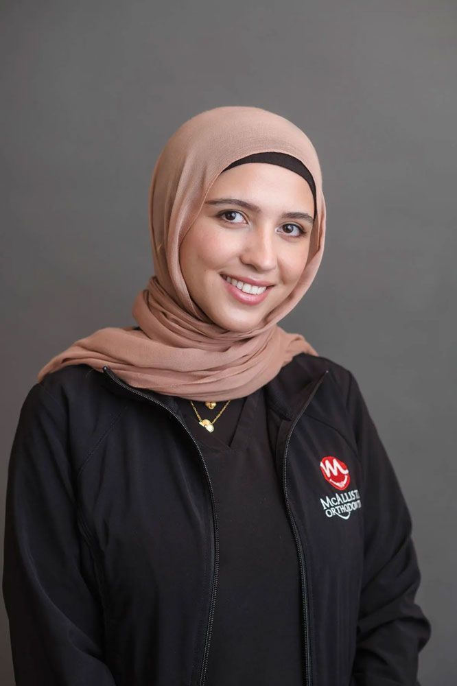 A woman wearing a hijab and a black jacket is smiling for the camera.