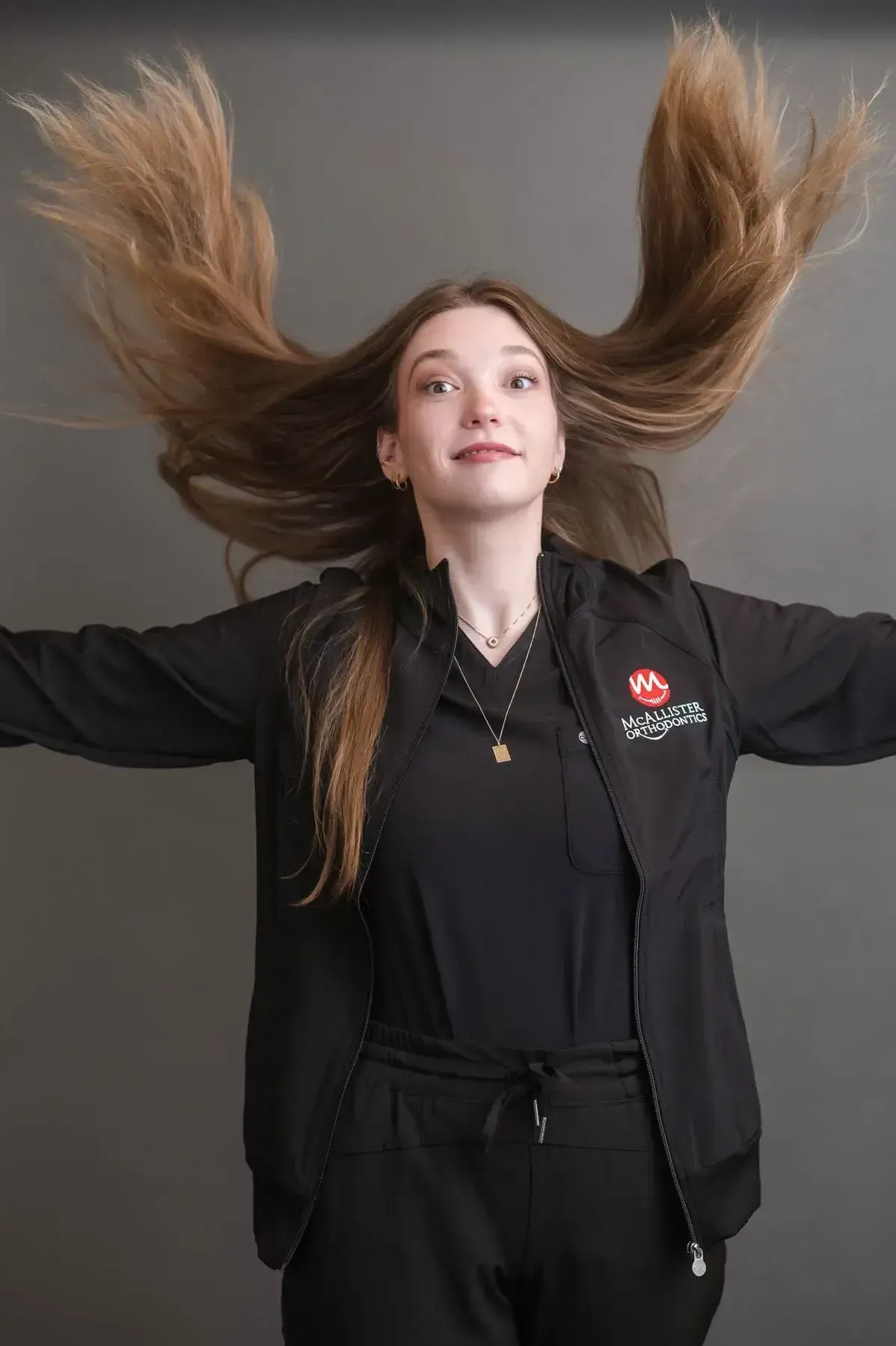 A woman with long hair is wearing a black jacket and standing with her arms outstretched.