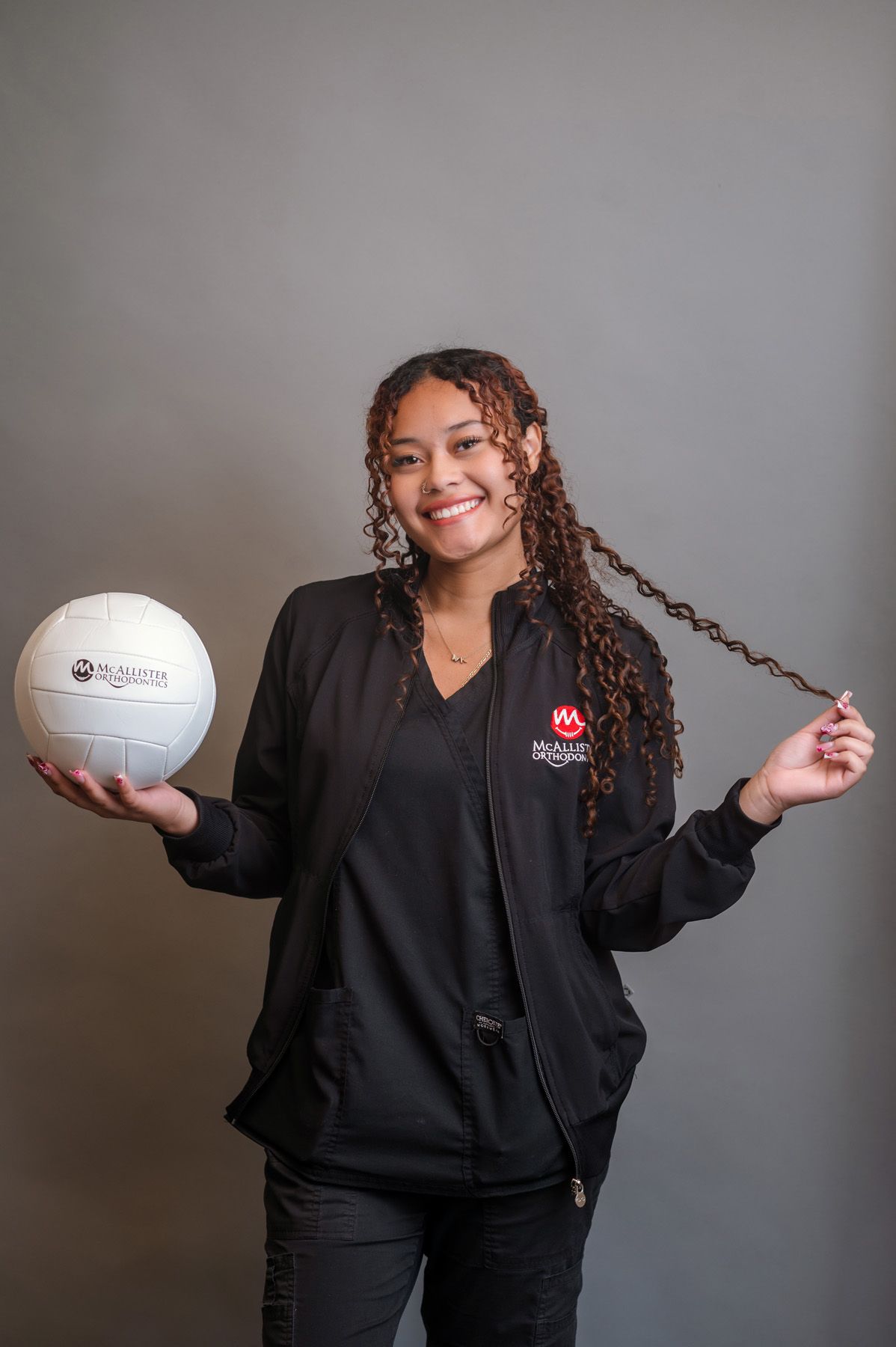 A woman in a black jacket is standing with her hands on her hips and smiling.