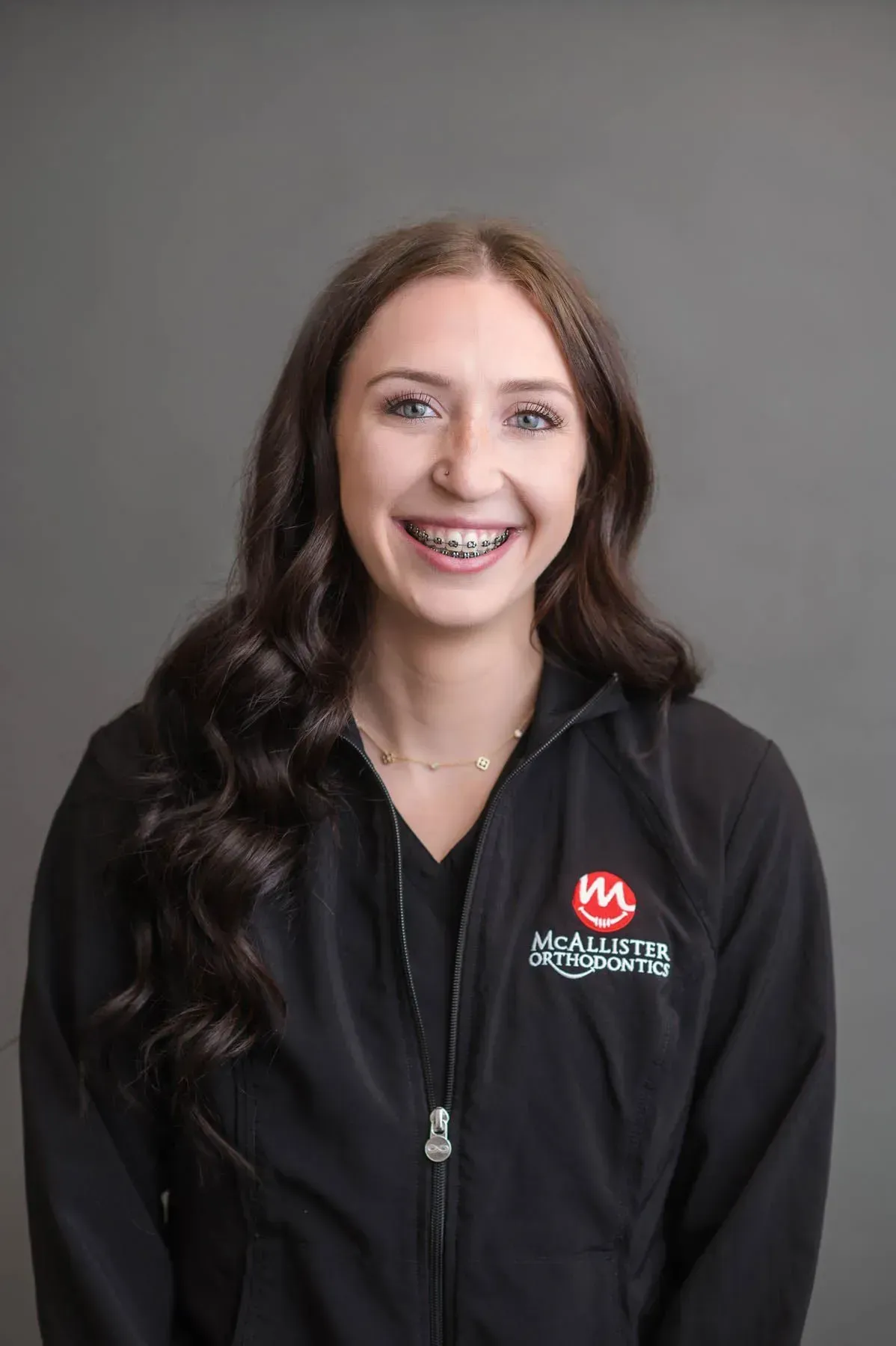 A woman wearing braces and a black jacket is smiling for the camera.