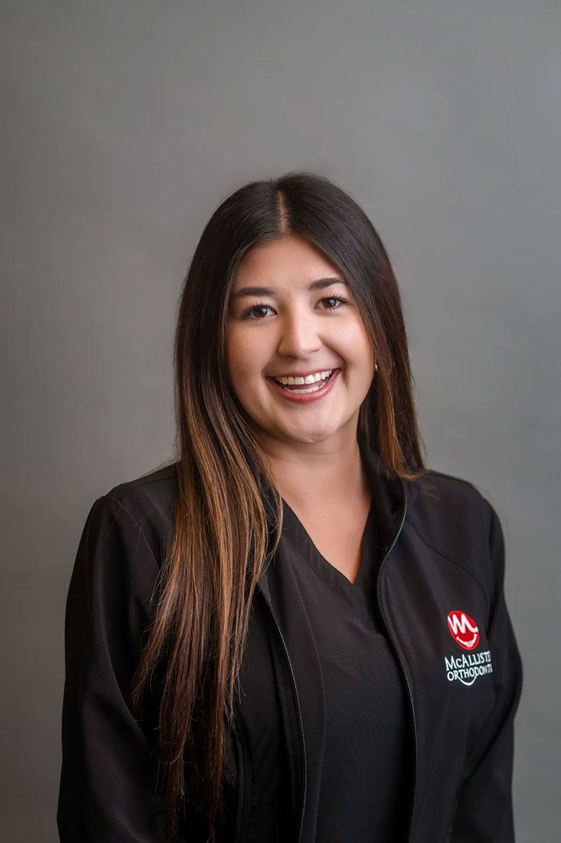 A woman with long hair is wearing a black jacket and smiling for the camera.