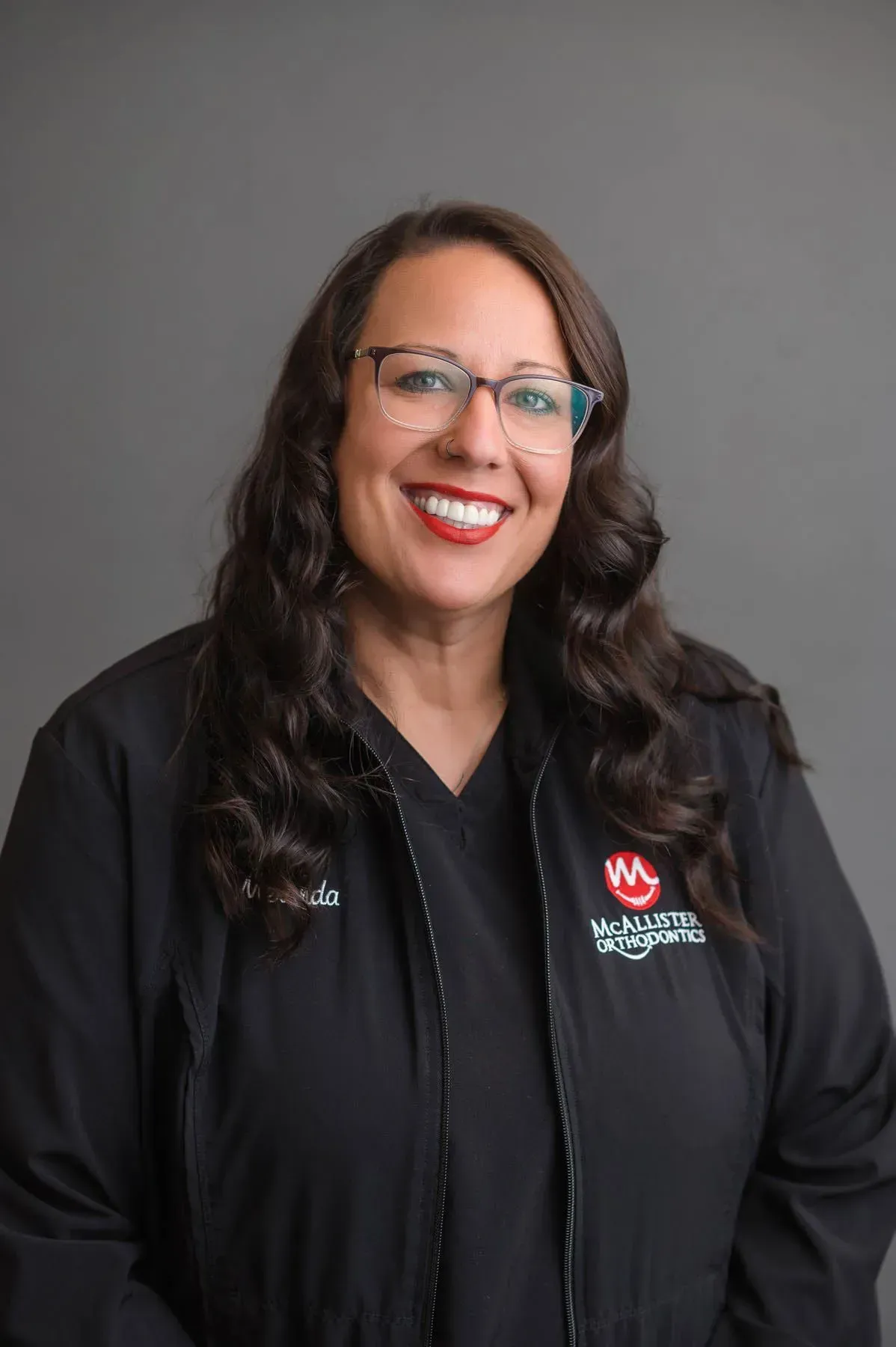 A woman wearing glasses and a black jacket is smiling for the camera.