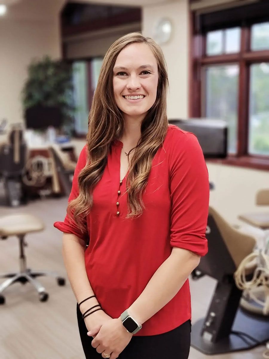 A woman in a red shirt is standing in front of a window.