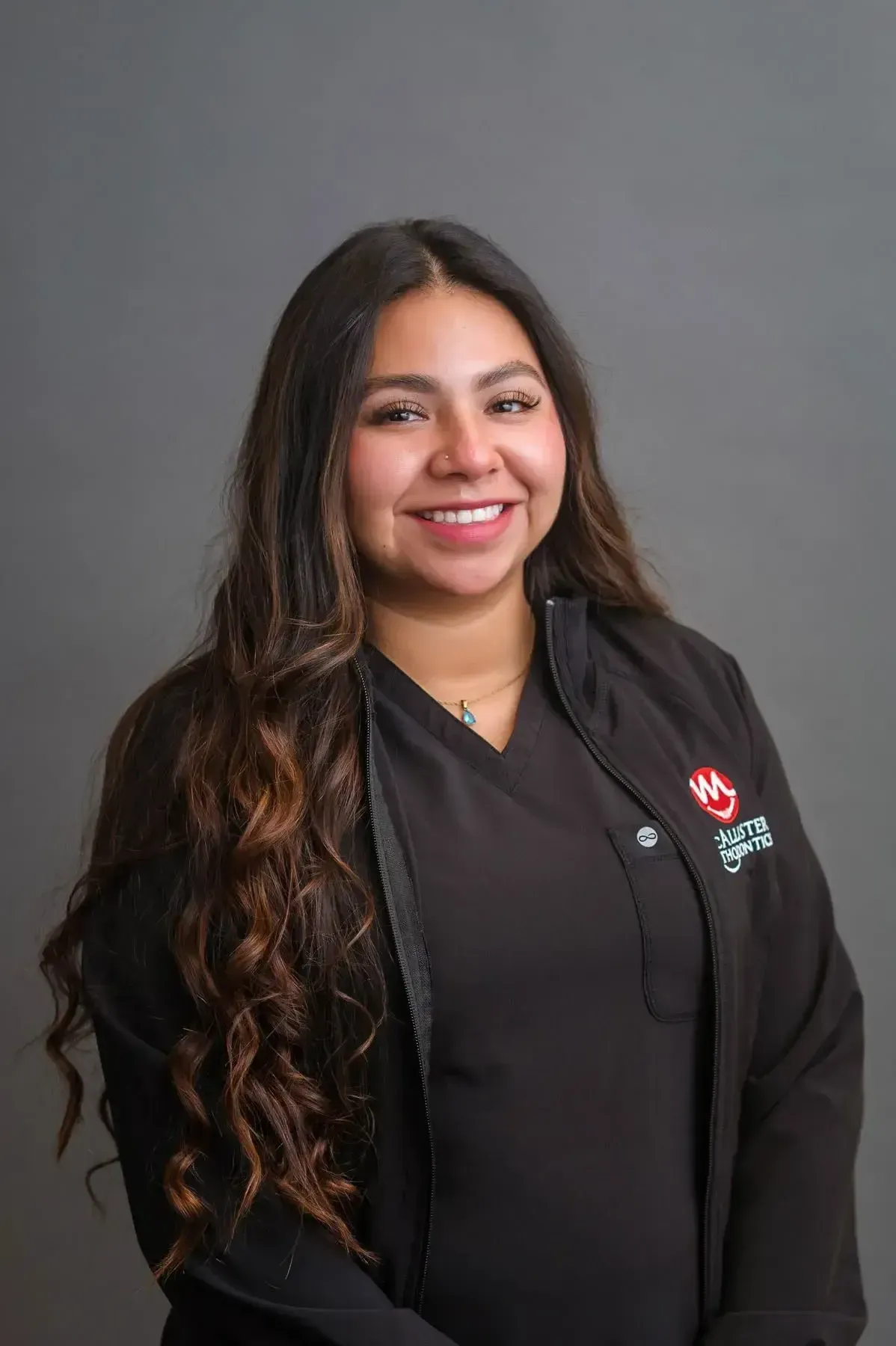 A woman with long hair is wearing a black jacket and smiling for the camera.