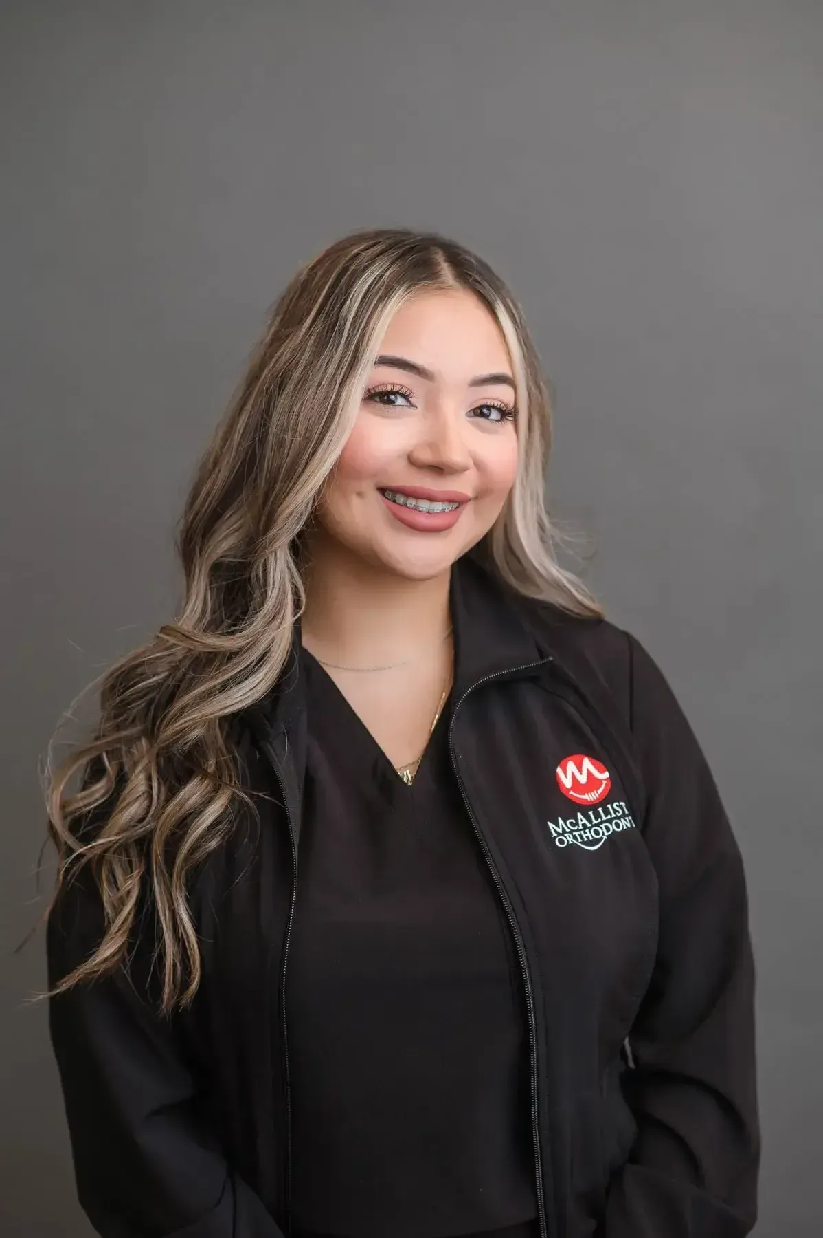 A woman wearing braces and a black jacket is posing for a picture.