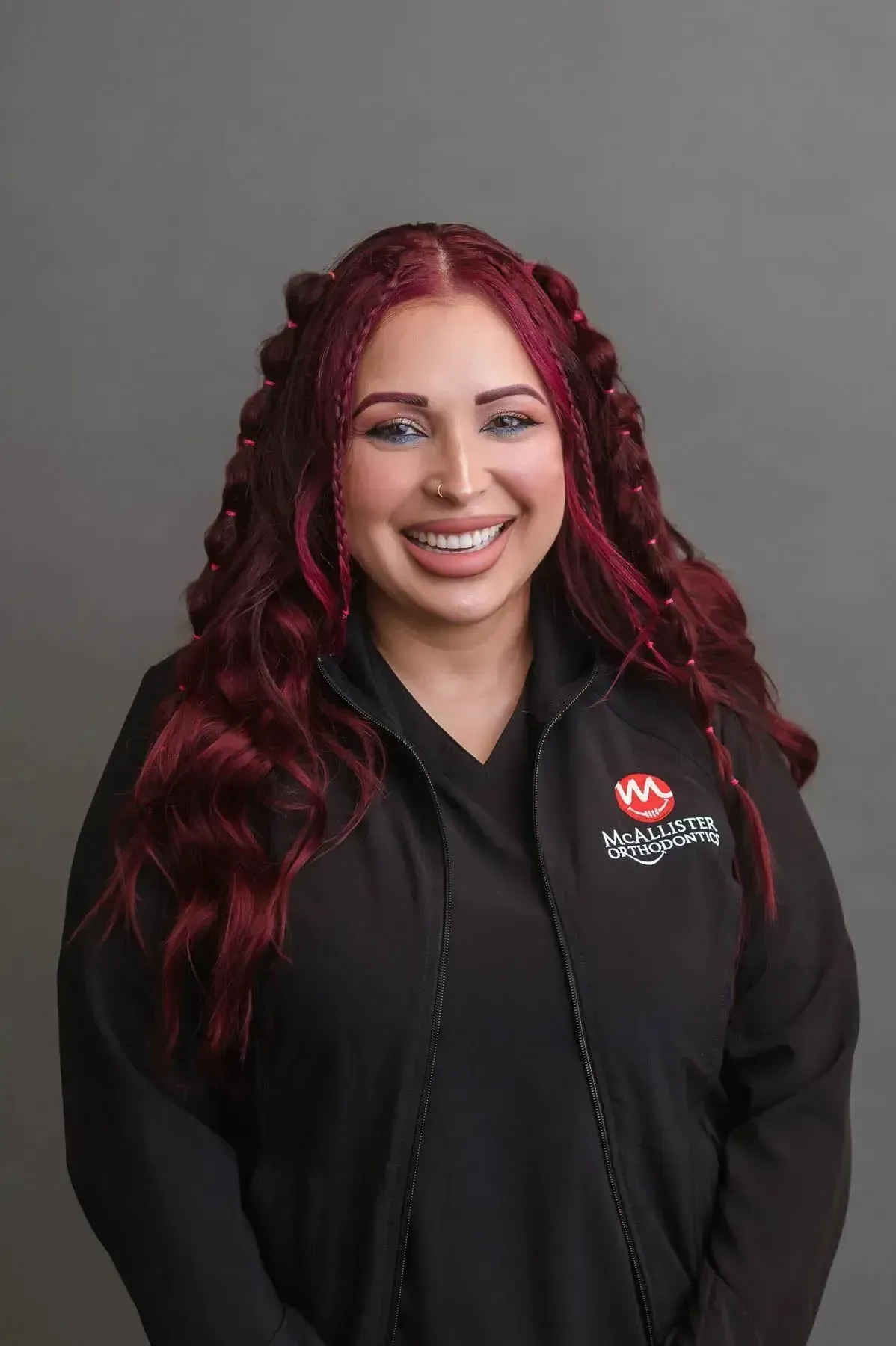 A woman with red hair is wearing a black jacket and smiling.