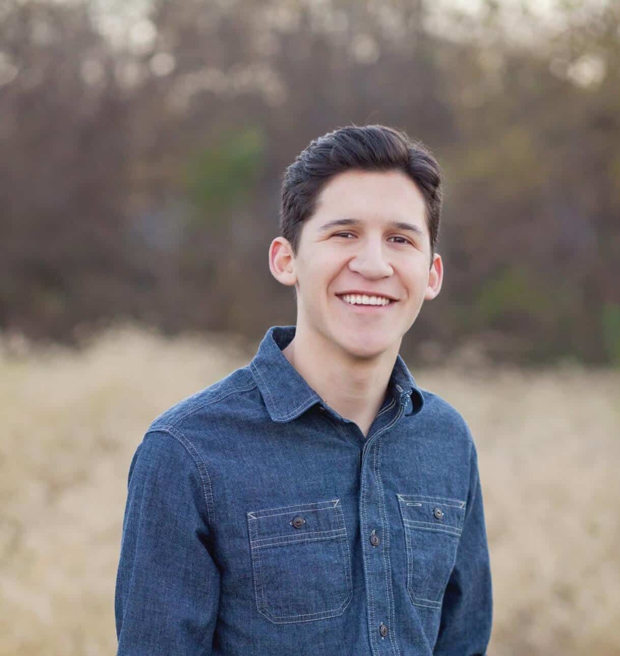 A young man in a denim shirt is smiling for the camera
