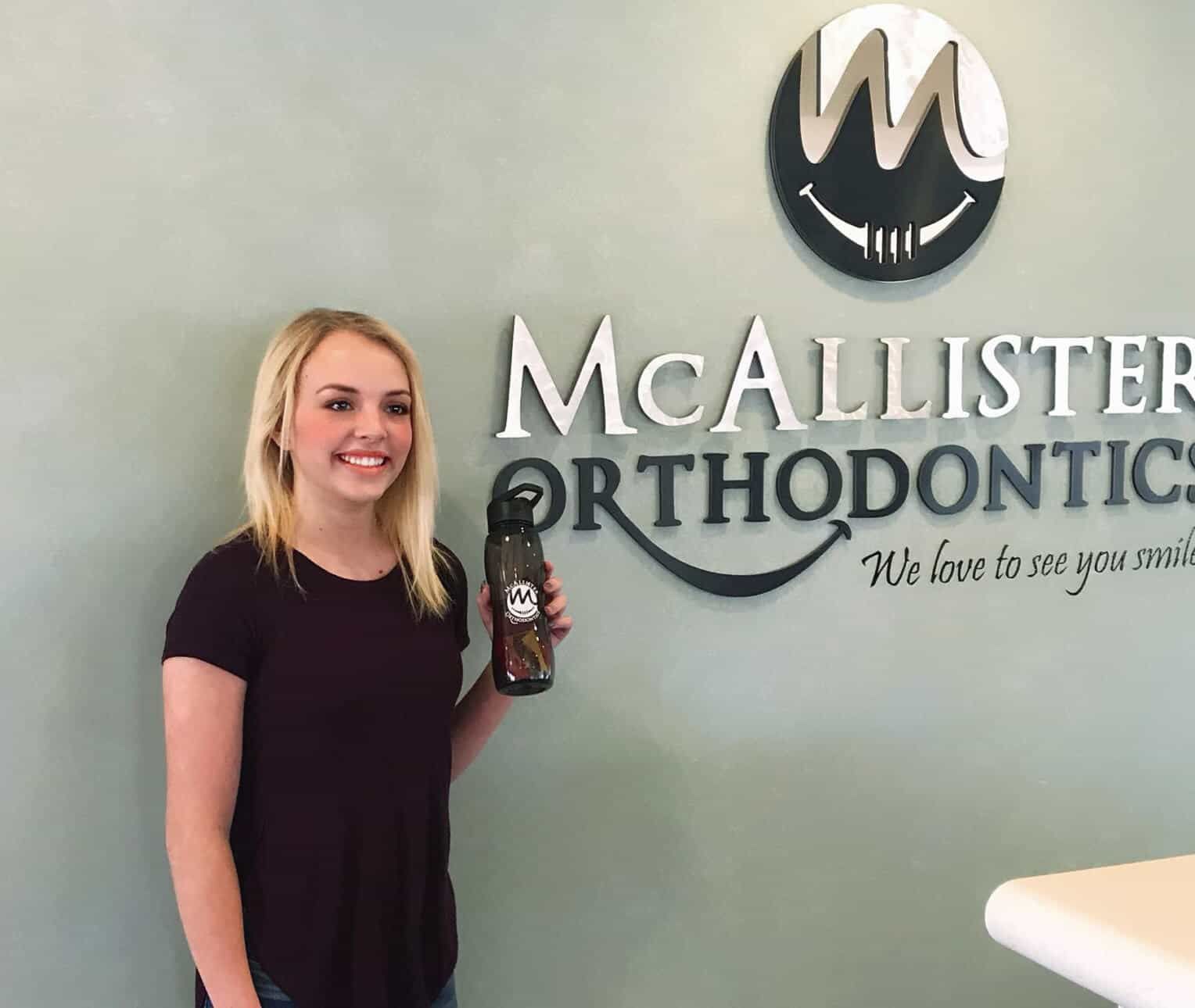 A woman is standing in front of a sign for McAllister orthodontics