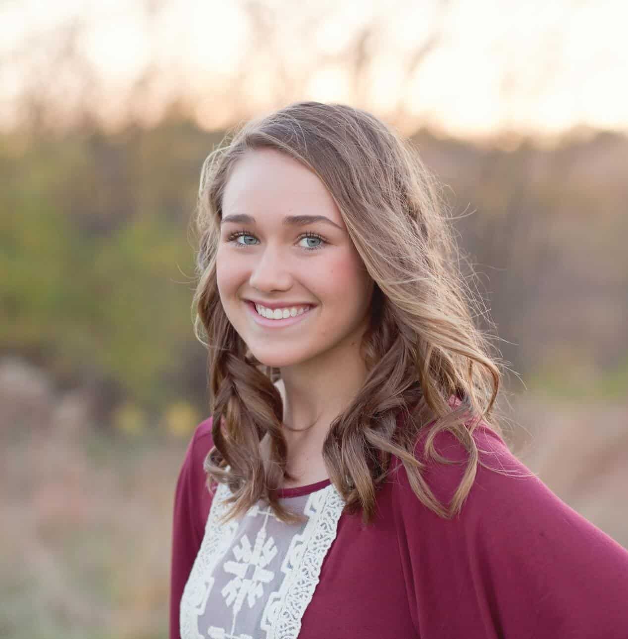 A young woman wearing a red sweater and a white lace top is smiling for the camera.