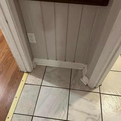 A corner of a room with a tiled floor and a wooden wall.