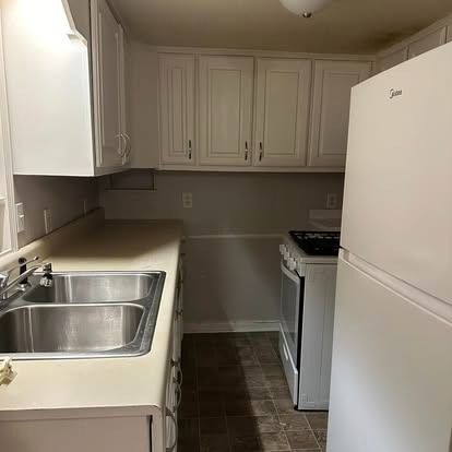 A kitchen with a sink , stove , refrigerator and cabinets.