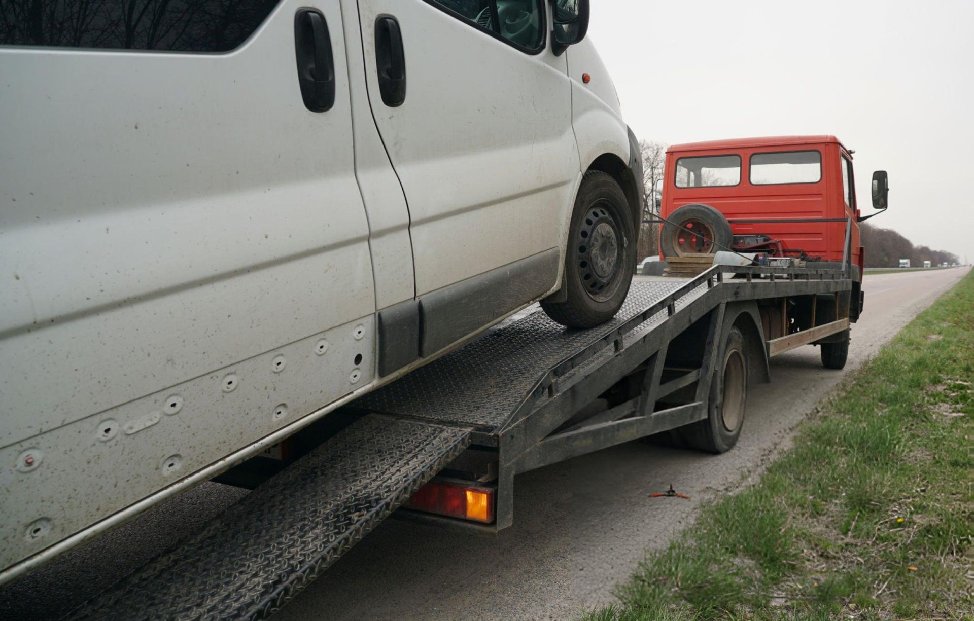 White van being loaded onto a flatbed tow truck on the side of a road; tow truck is red.