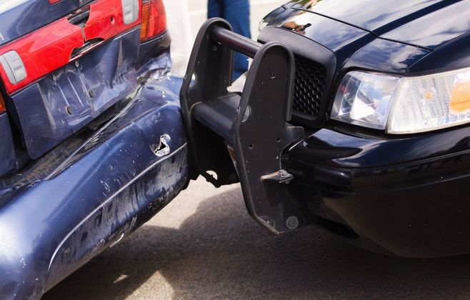 A black car with a bull bar has crashed into the rear of a blue car, both heavily damaged, on asphalt.