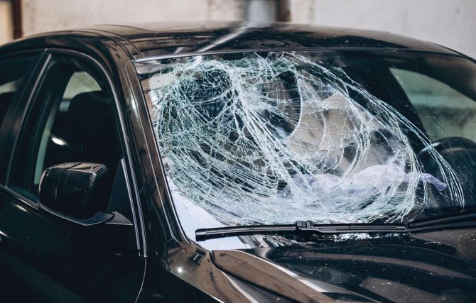 A black car with a shattered windshield; the glass is spiderwebbed with cracks.