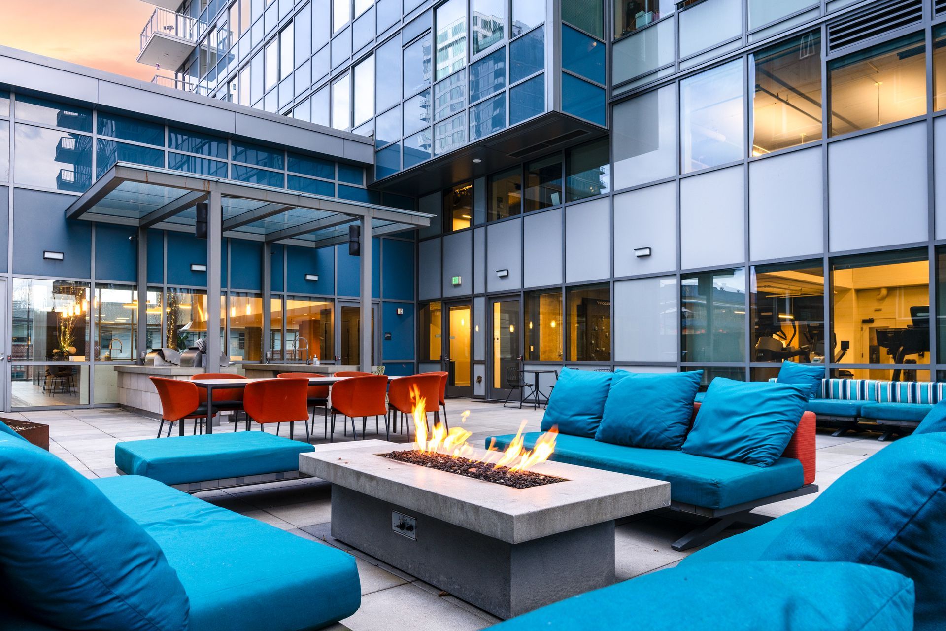 A patio with blue furniture and a fire pit in front of a building.