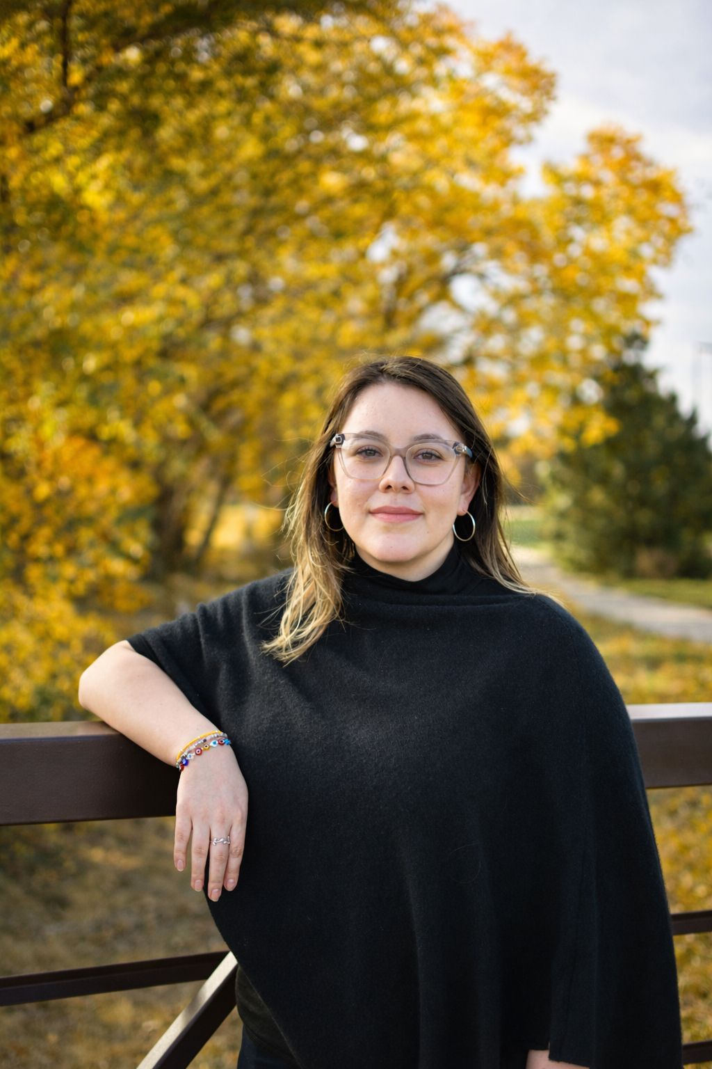 A smiling person with long brown hair wearing a dark blue and gold academic robe and red tassel earrings.