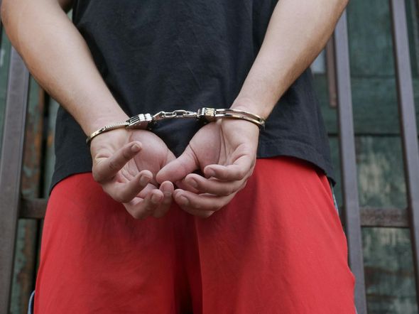 Person wearing handcuffs behind their back, standing in a black shirt and red shorts.