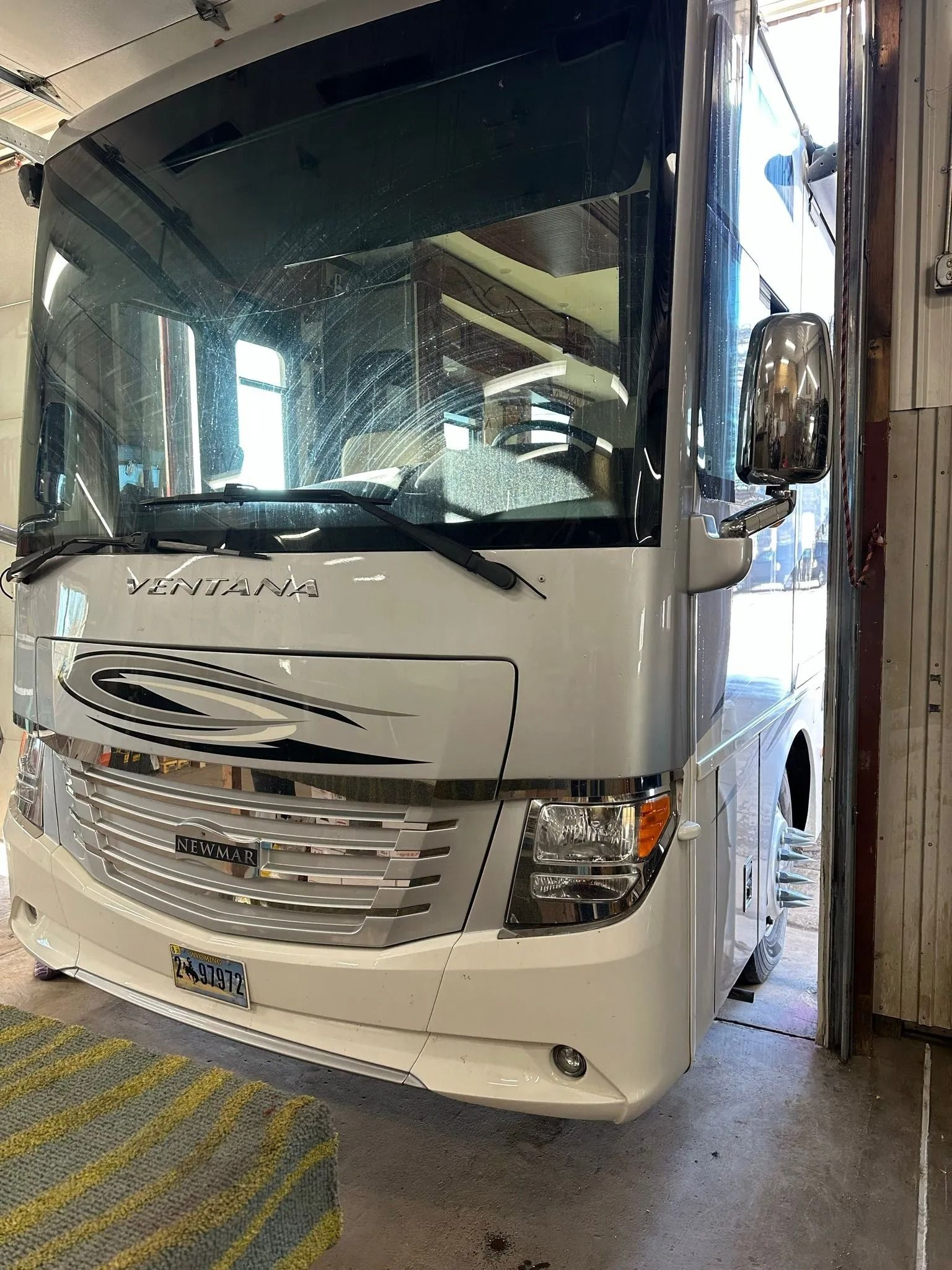 A white motorhome parked inside a garage, viewed from the front, featuring a large windshield, headlights, and grille.