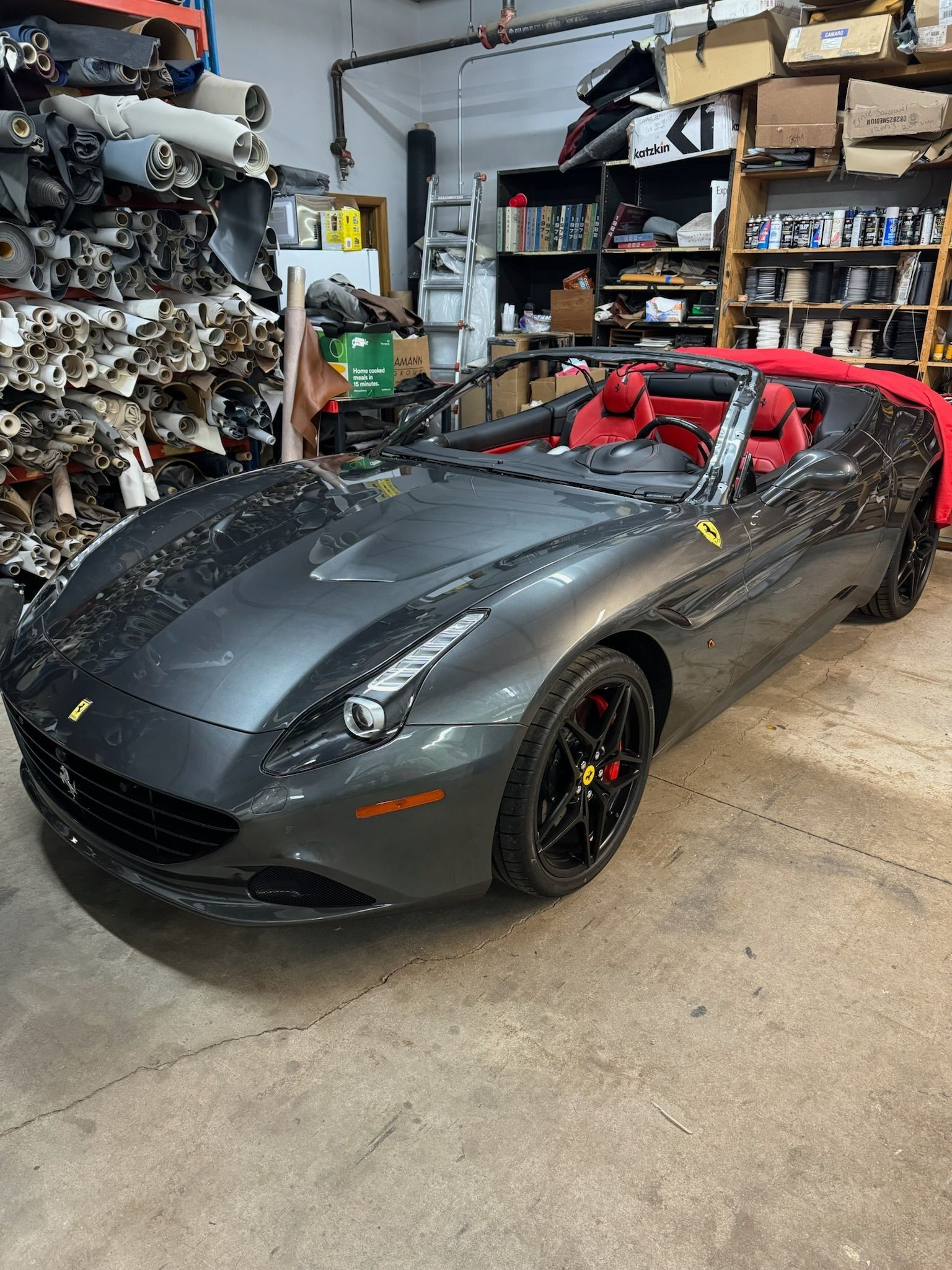 A gray Ferrari convertible with red leather interior parked in a cluttered automotive garage.