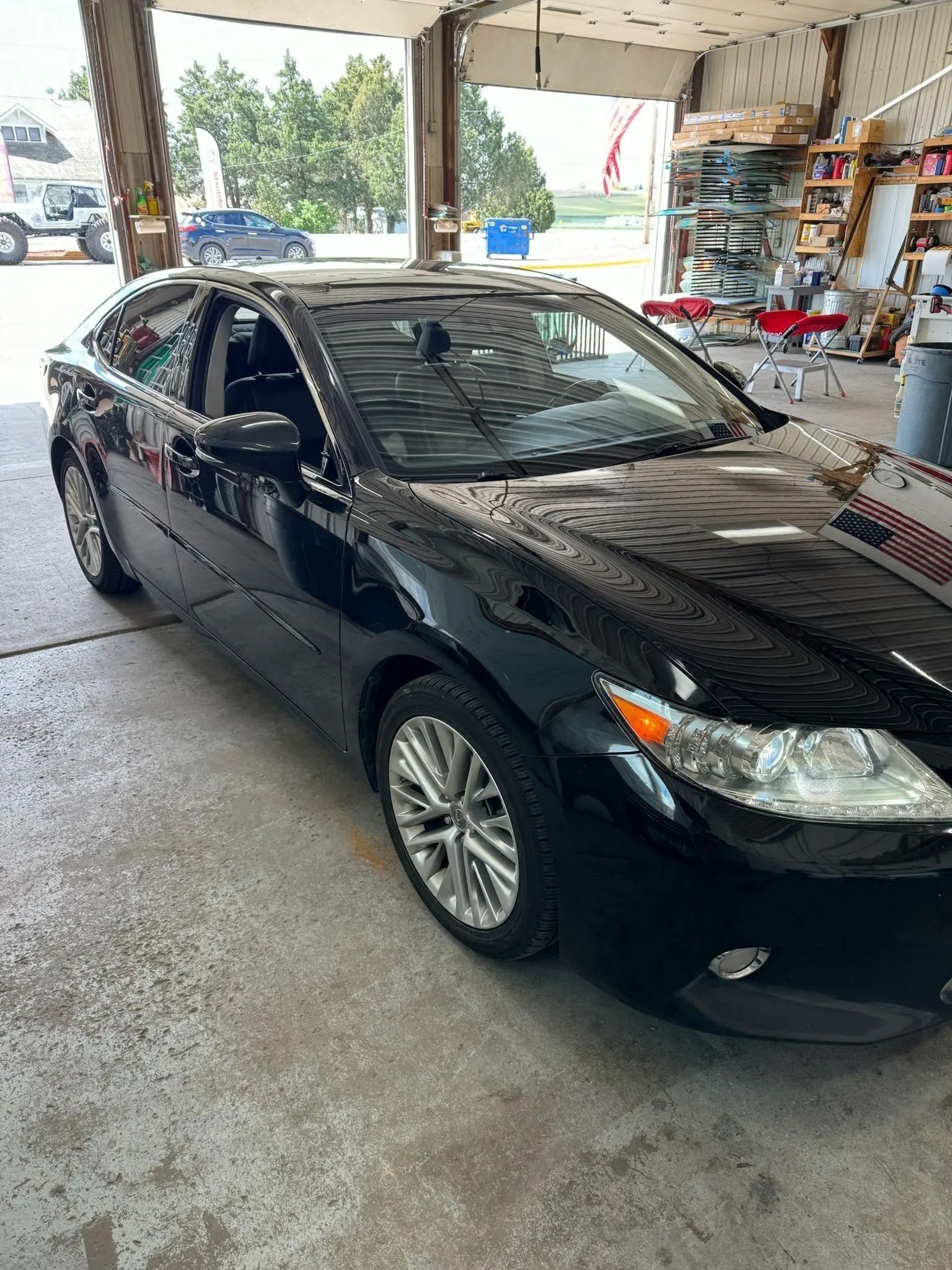 A sleek black sedan parked inside a well-lit auto repair shop with work tables and tools visible in the background.