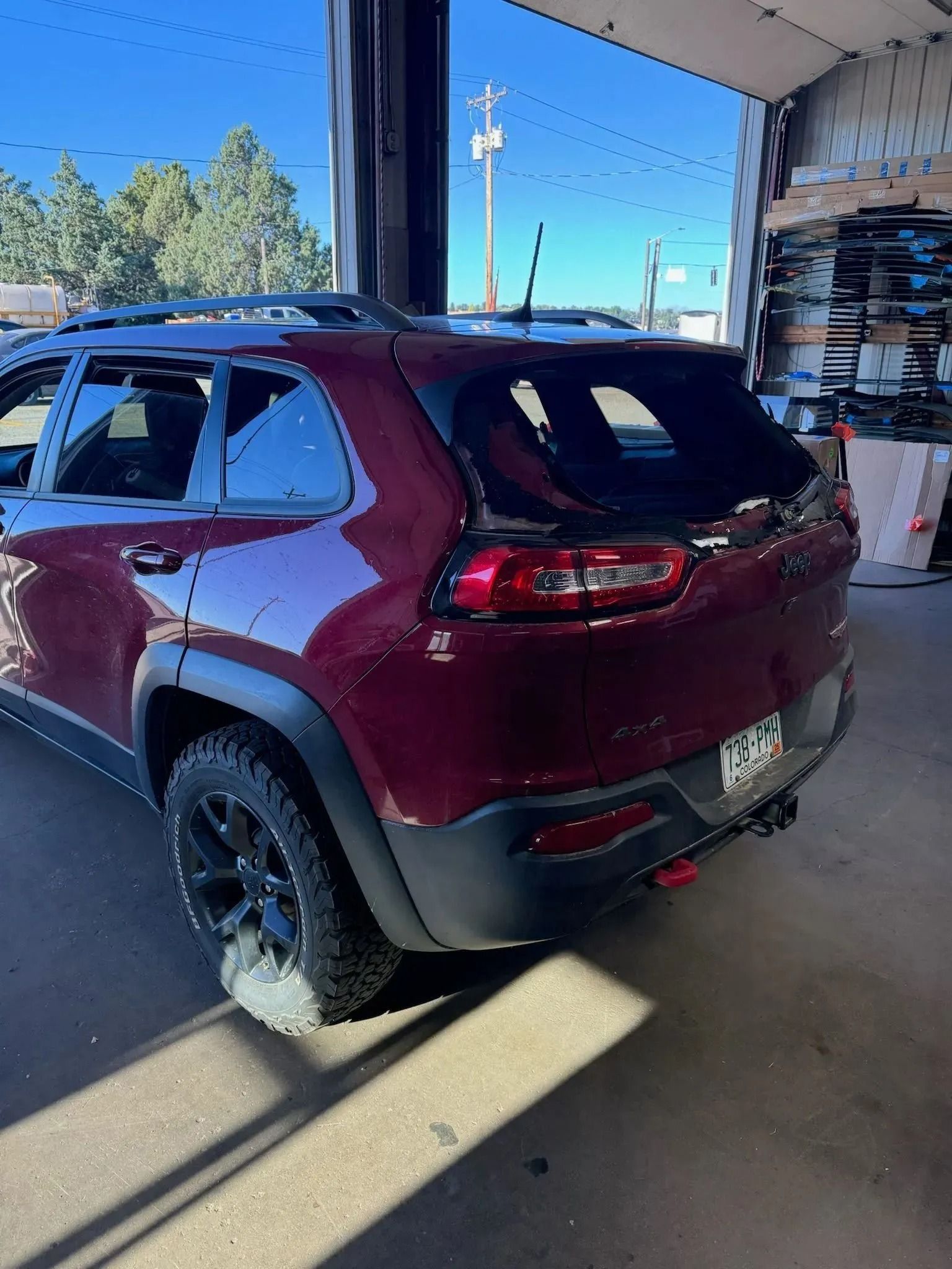 A maroon Jeep Cherokee SUV parked inside a garage, viewed from the rear, showing its back window and taillight.