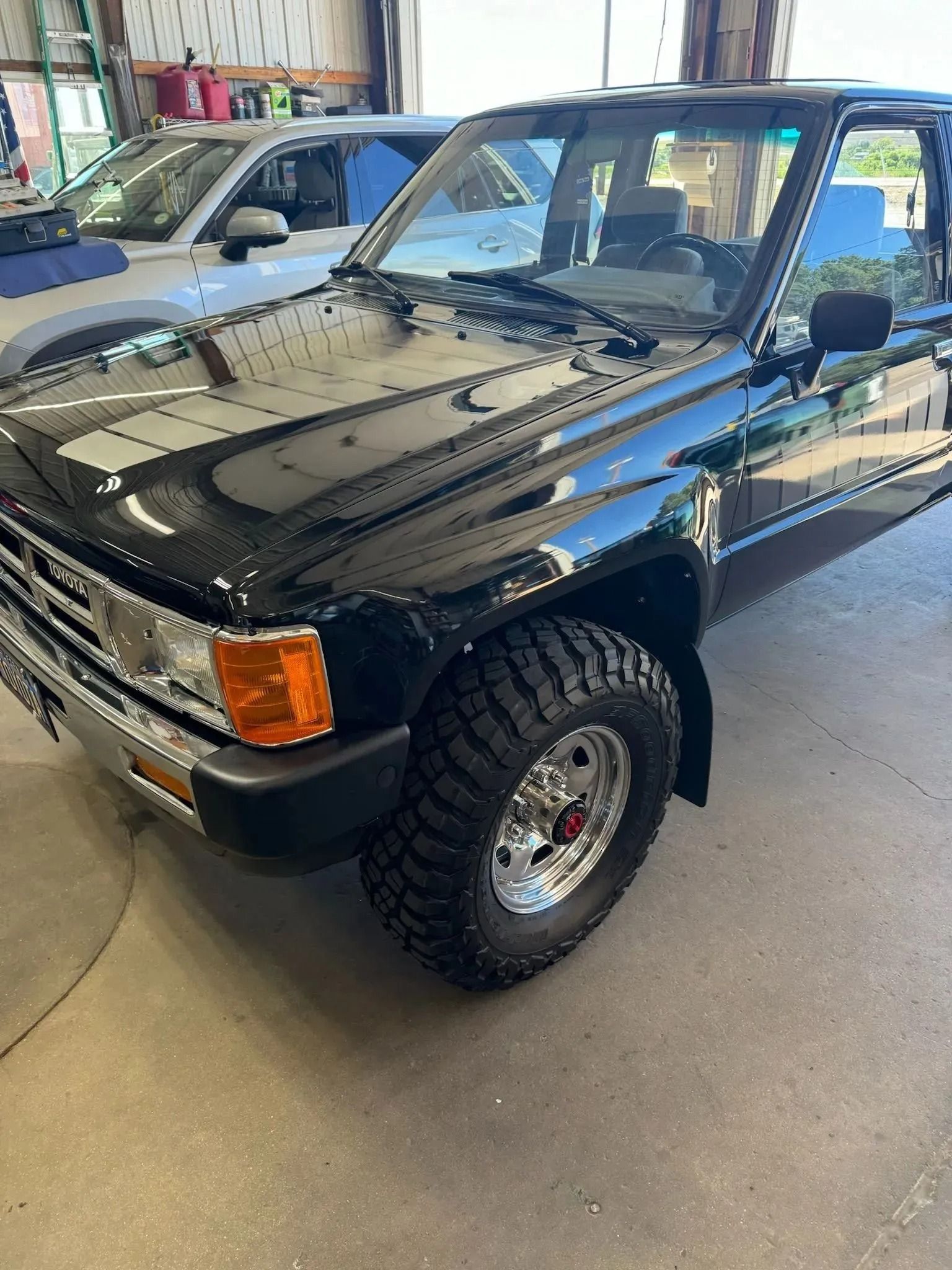 A clean, black Toyota pickup truck with large off-road tires parked inside a garage.