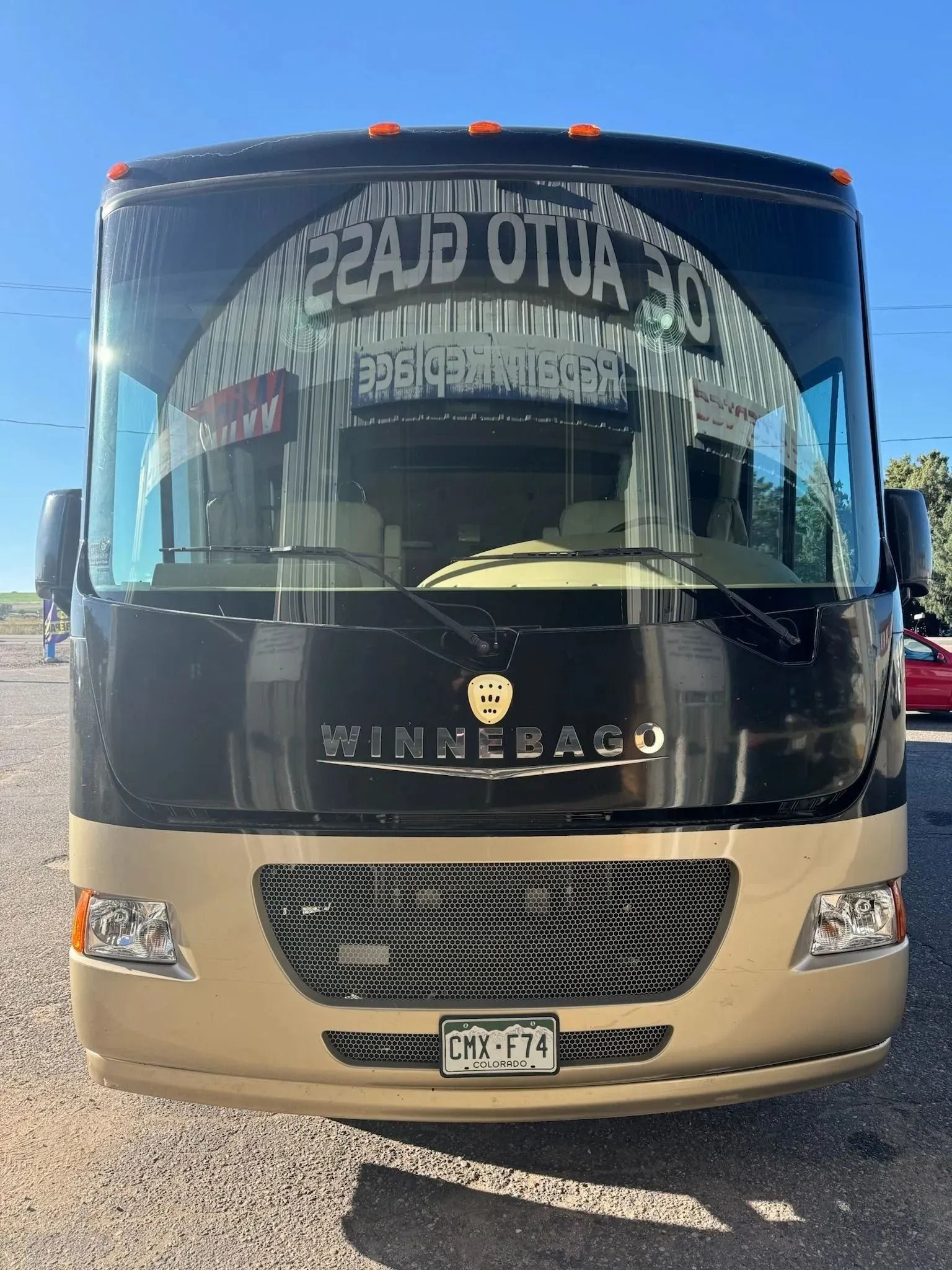 A front view of a black and tan Winnebago motorhome parked outdoors against a clear blue sky.