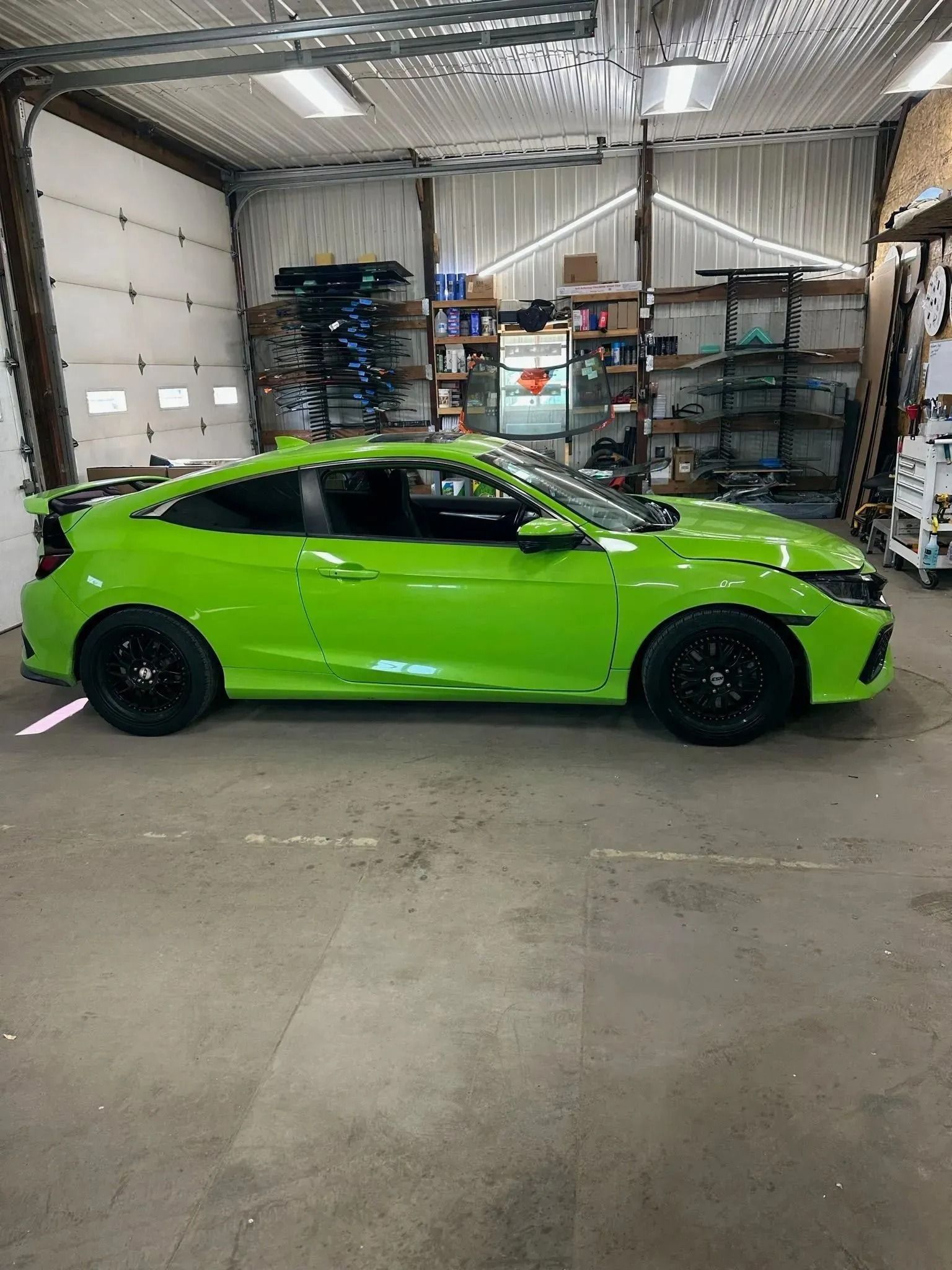 A bright green Honda Civic coupe parked inside a workshop with storage shelving in the background.