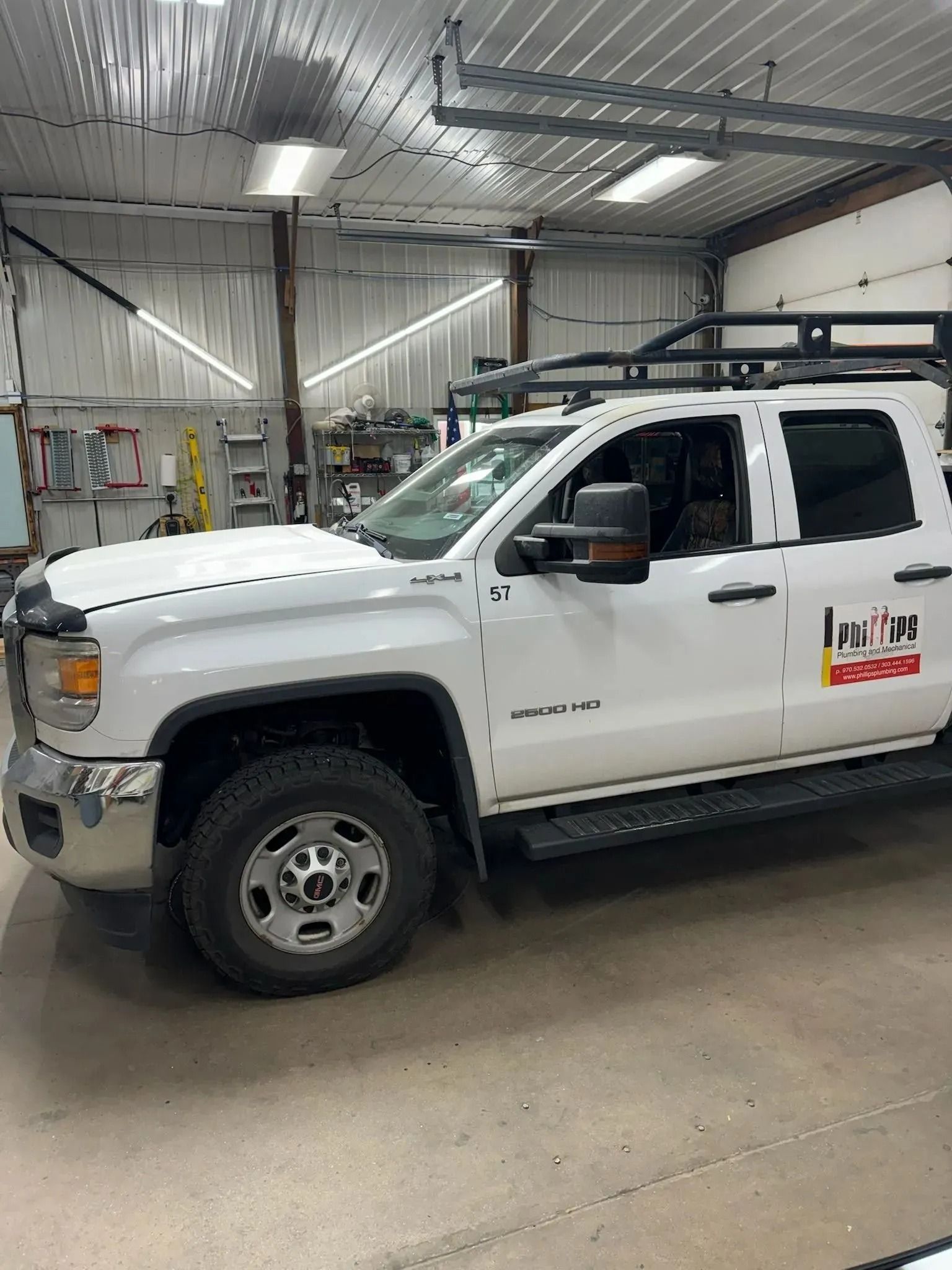 A white GMC pickup truck with a roof rack and company logo parked inside a garage.