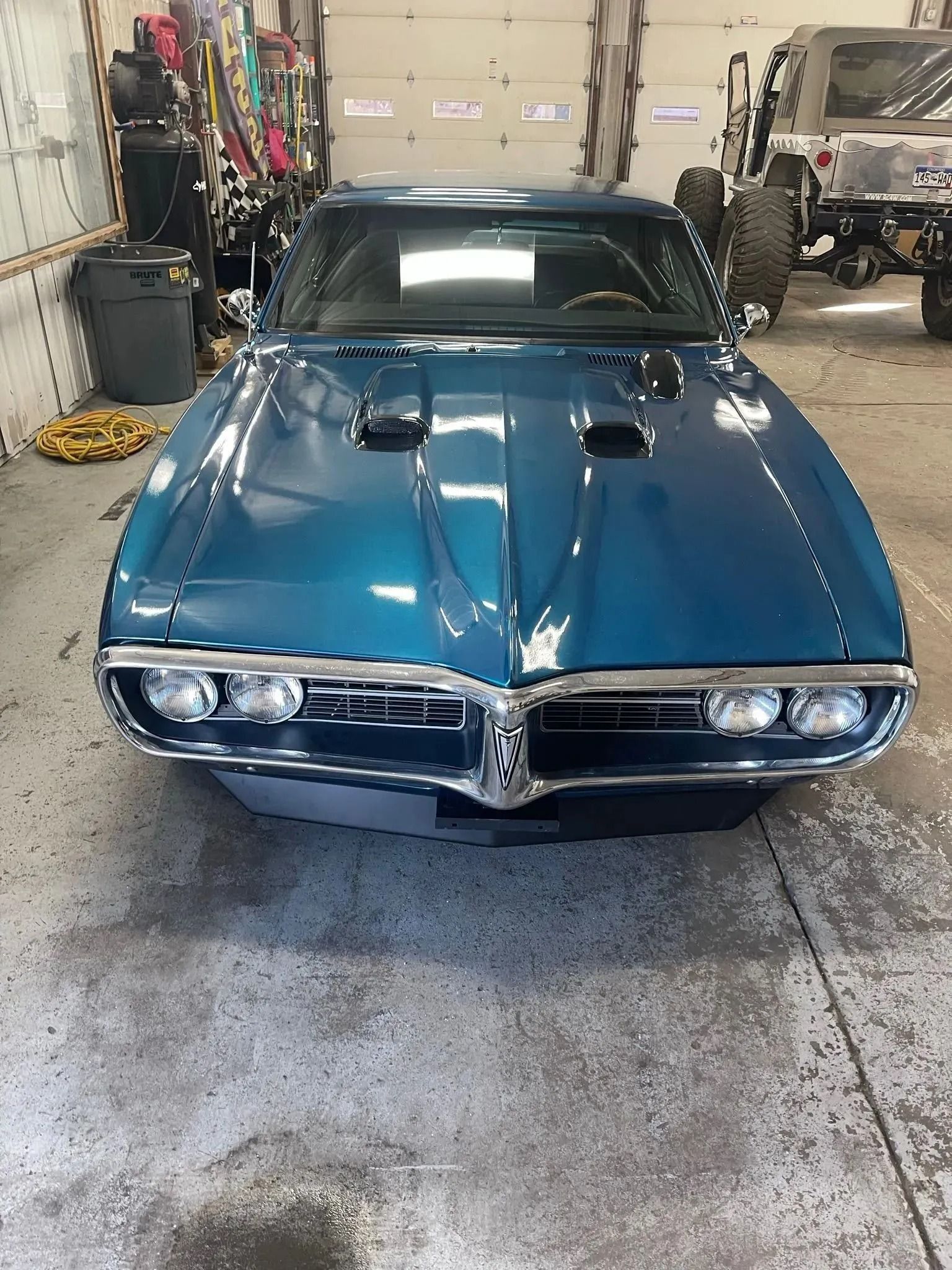 A teal Pontiac Firebird parked inside a garage, facing forward.