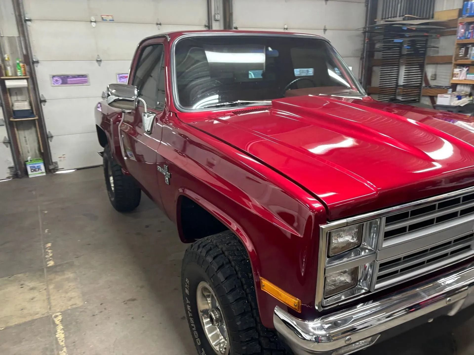 A red vintage Chevrolet pickup truck parked inside a workshop with a chrome front grille and bumper.