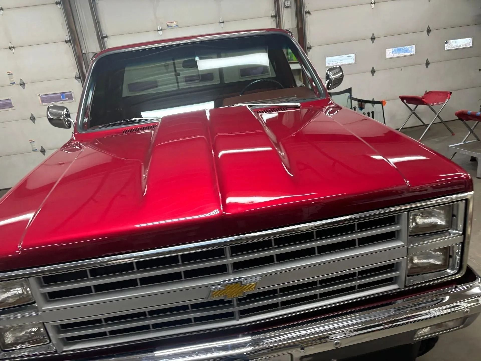 A shiny red Chevrolet truck with a cowl induction hood parked inside a garage.