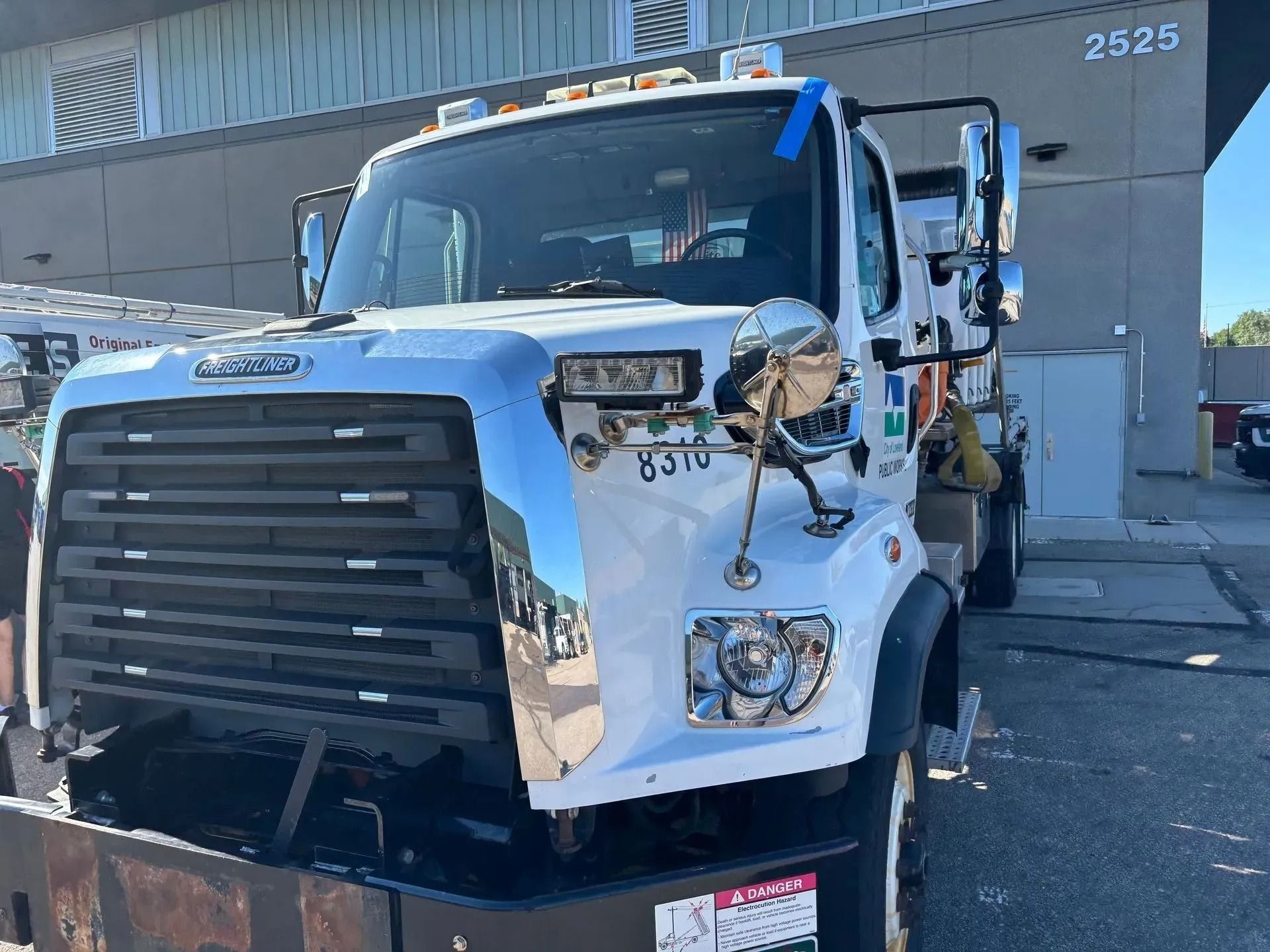 A white Freightliner service truck parked in a paved lot in front of a building with the number 2525.
