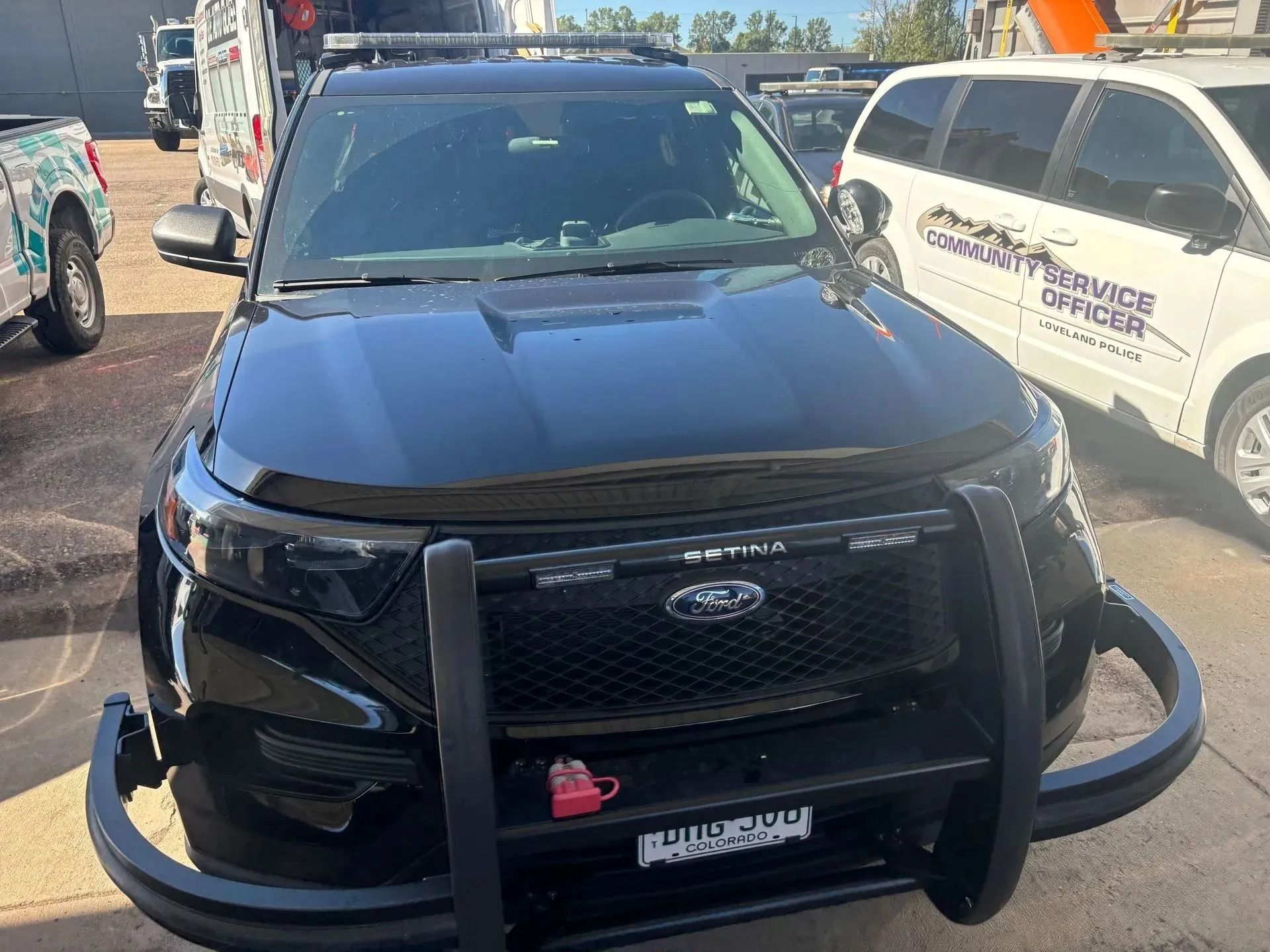 A black Ford police interceptor SUV with a front brush guard parked in a lot next to a community service officer van.