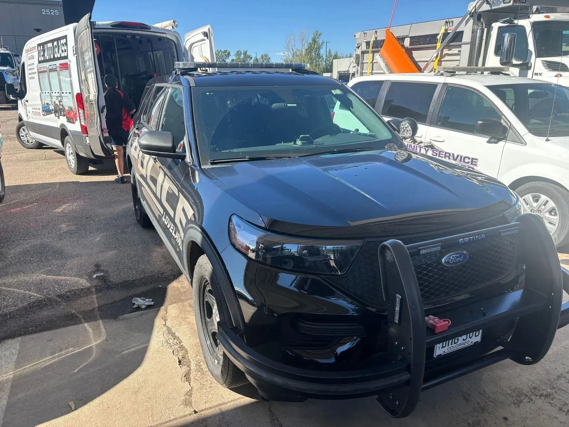 A black police SUV with a front brush guard parked in a lot next to a white service van and a white vehicle.
