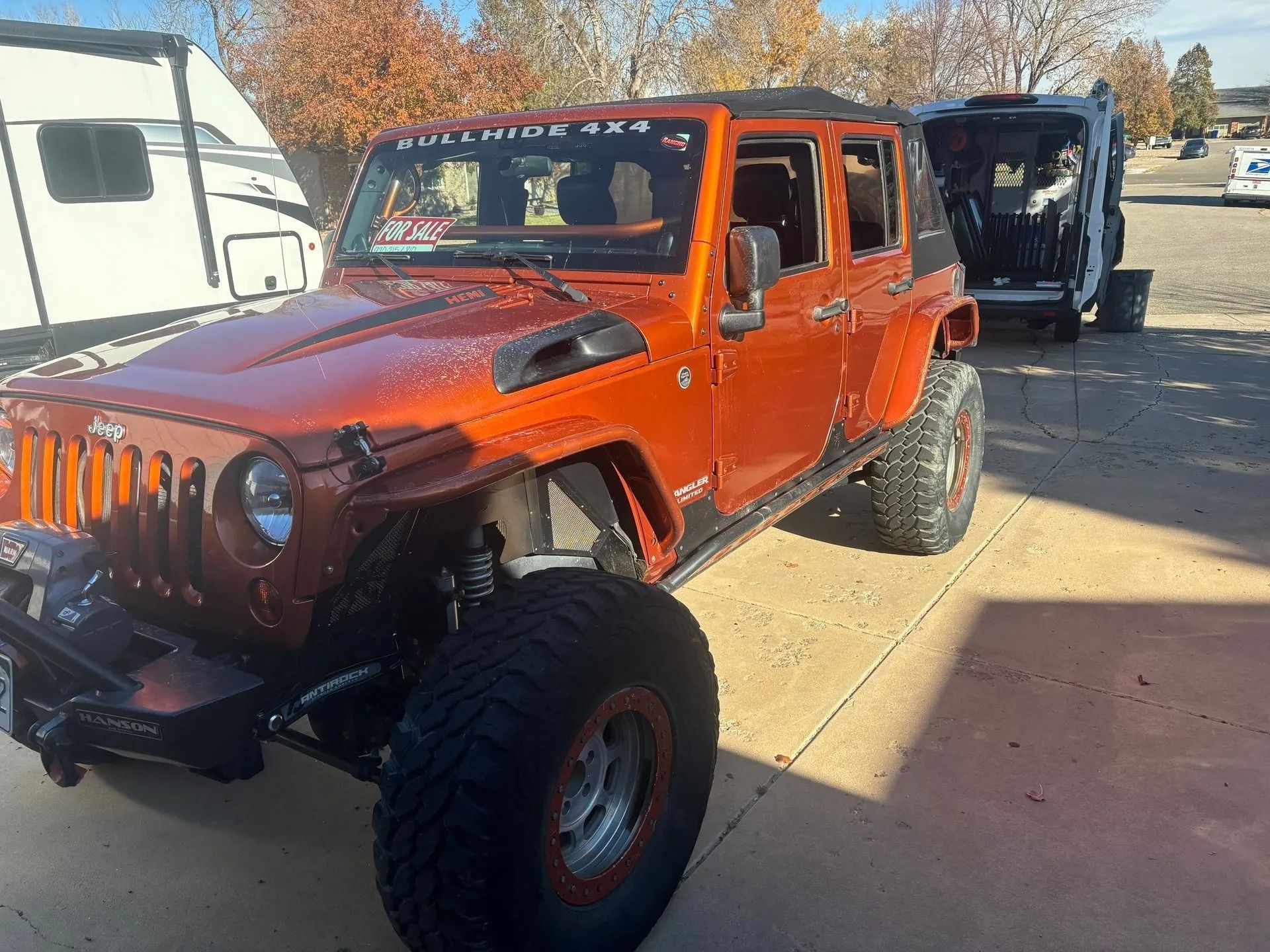 A bright orange, lifted Jeep Wrangler parked on a concrete driveway during the day.